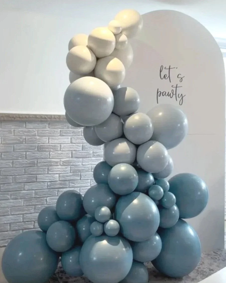 Decorative display of various-sized white and blue balloons arranged in a cluster against a white wall, with the phrase 'let's party' written on the wall.