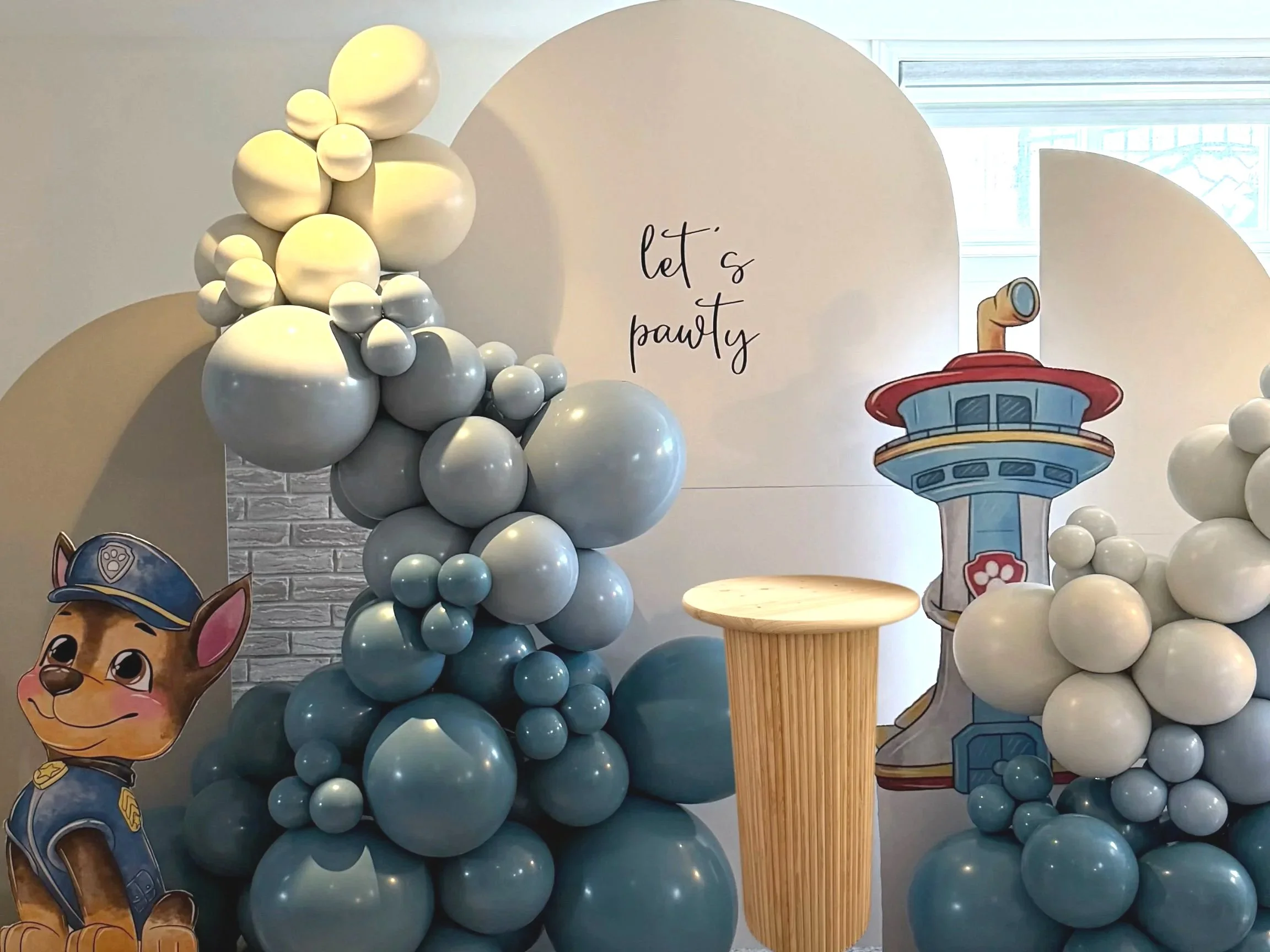 Balloon display with a paw patrol themed backdrop, including a cartoon dog character and a sky tower illustration, with the phrase 'let's party' written on the backdrop.