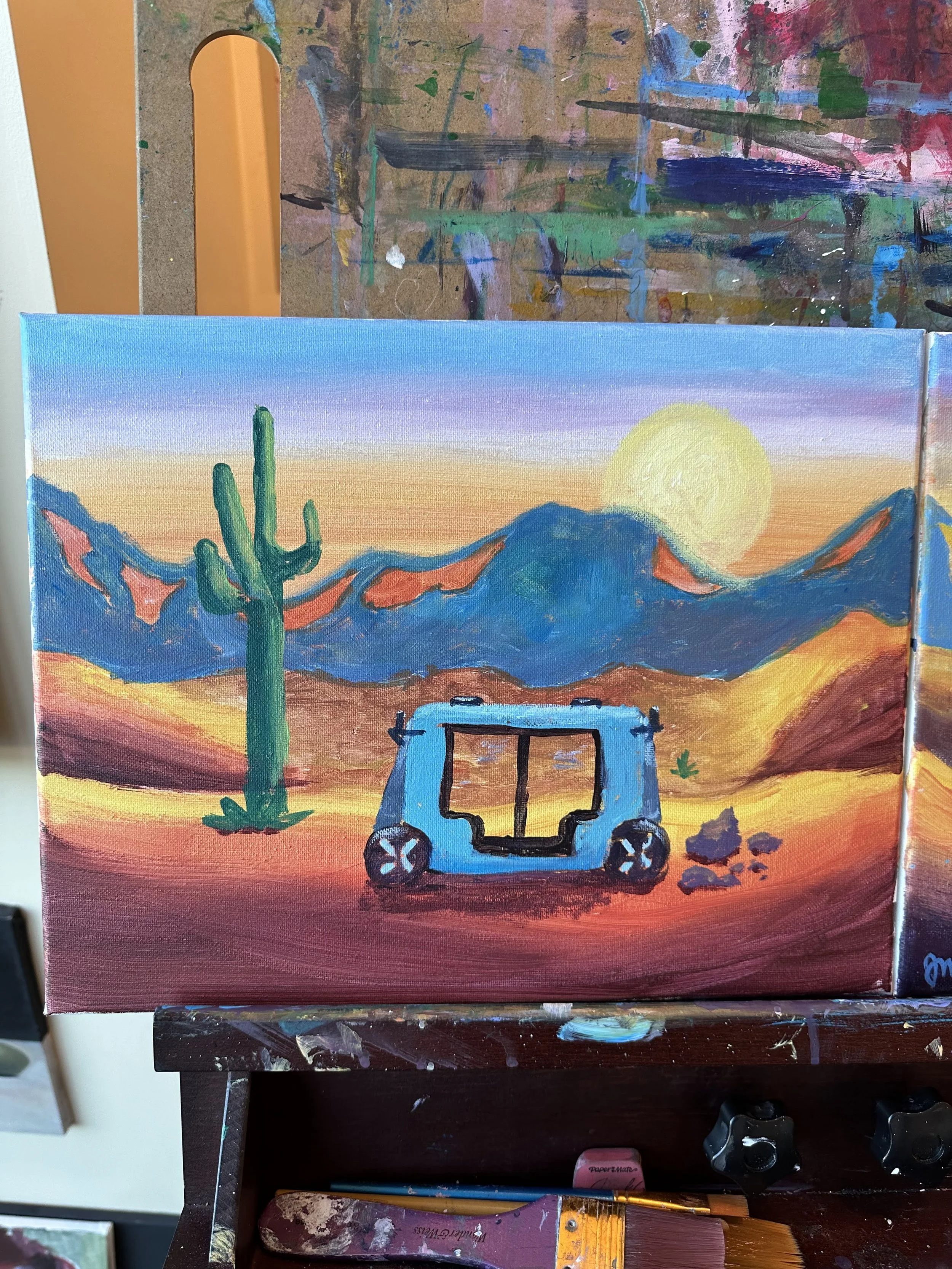 A colorful desert landscape painting depicting a blue RV, a green cactus, mountains, and a setting sun in the background.