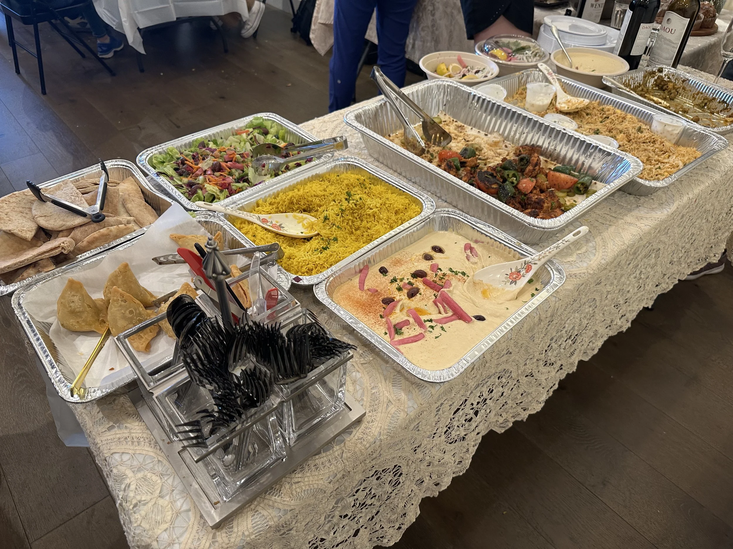 Buffet table with various dishes including salads, rice, and dips, set on a lace tablecloth at a dining event.