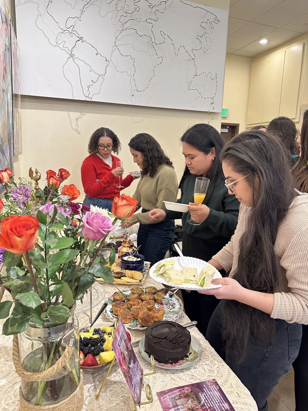 People gathered around a table with various desserts and flowers at a celebration or party.