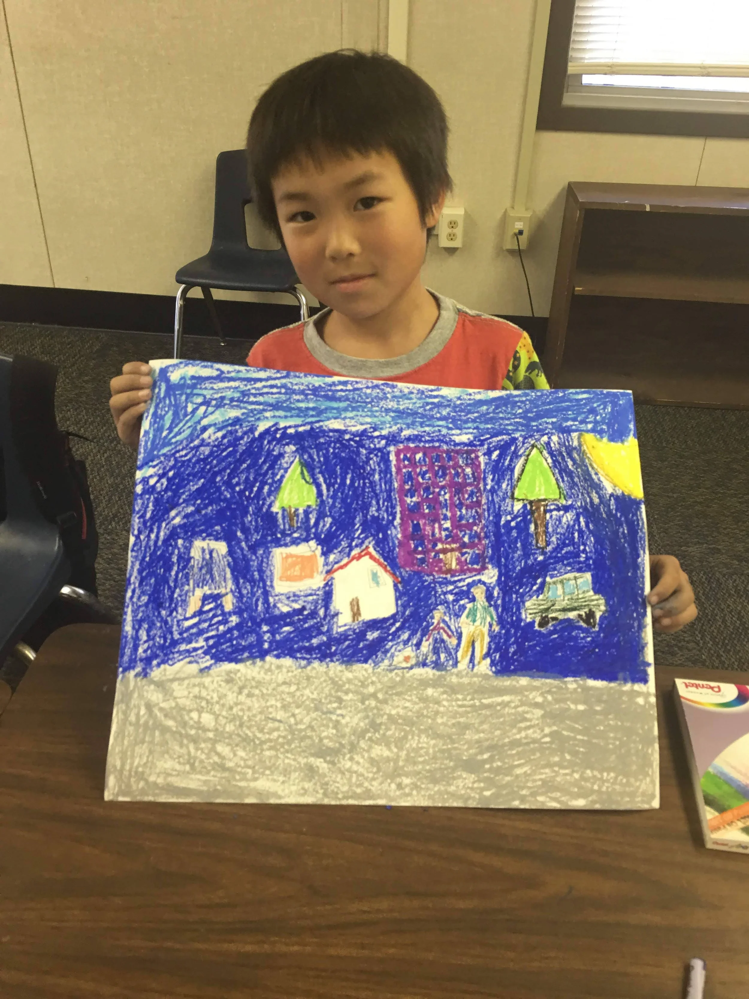 A young boy holding a colorful drawing of a cityscape with houses, trees, a car, and a person, against a blue sky with yellow moon.