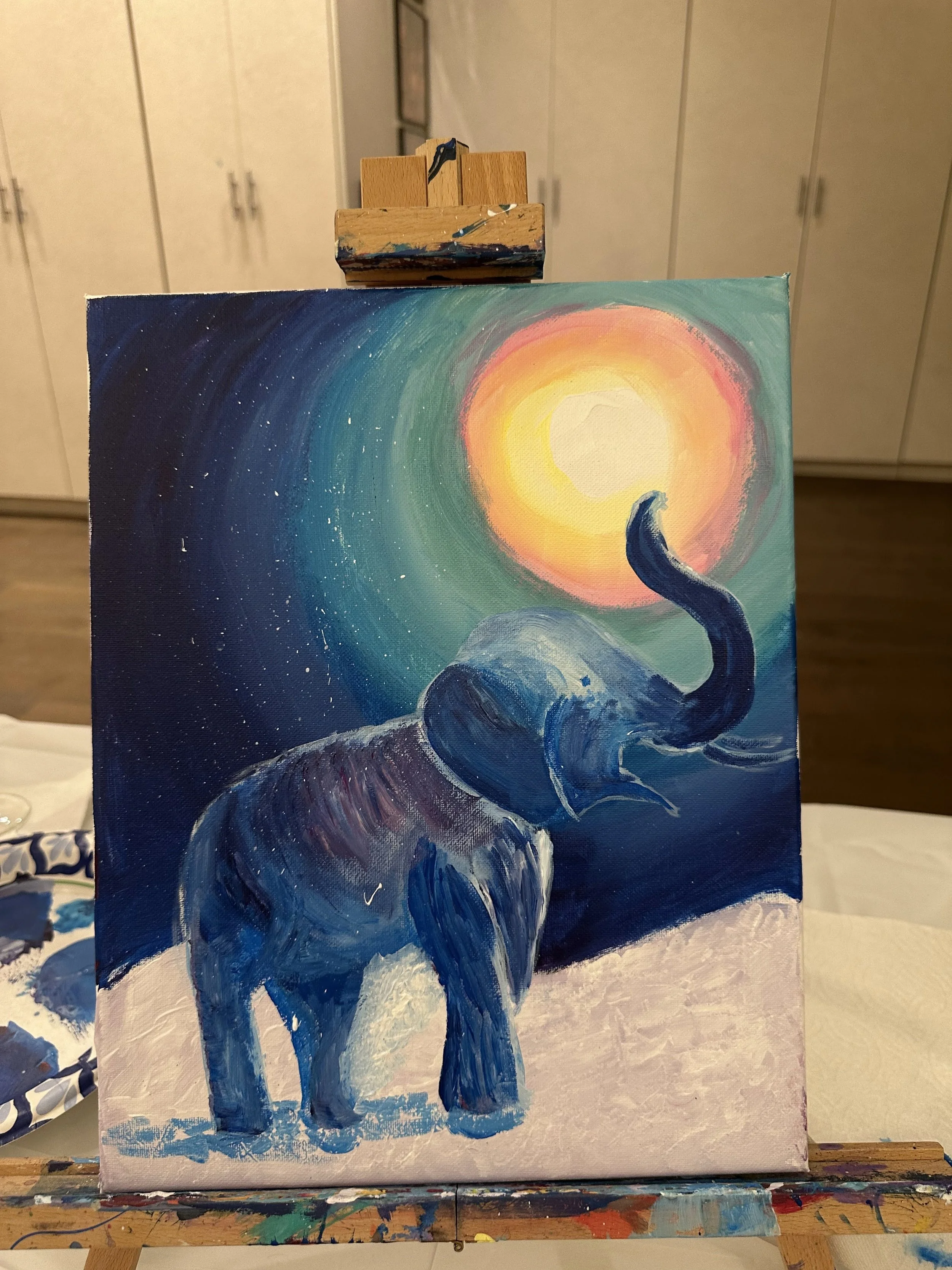 Painting of an elephant under a colorful sky with a bright sun.