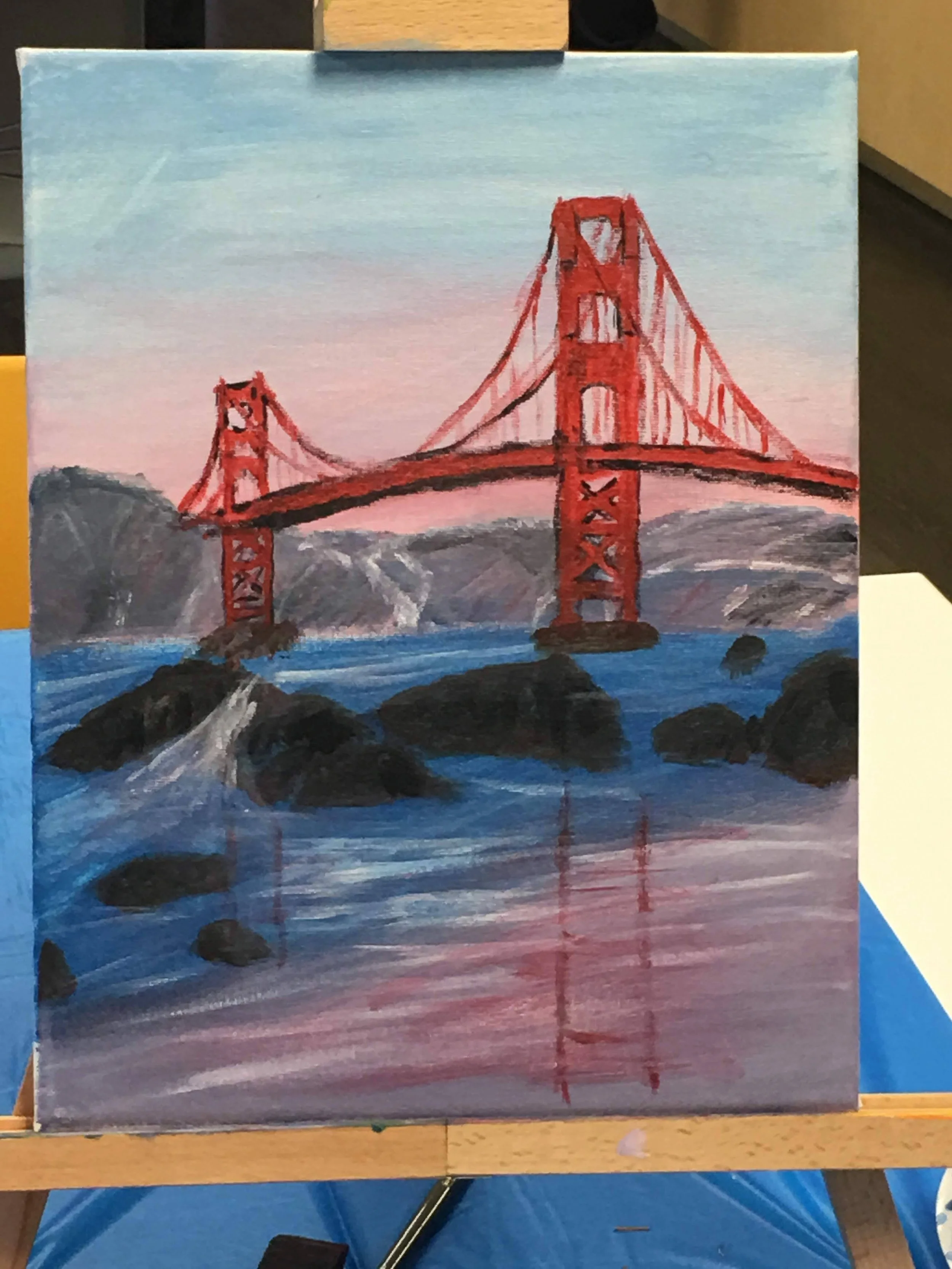 A painting of the Golden Gate Bridge over water with rocks in the foreground and hills in the background, under a pink and blue sky.