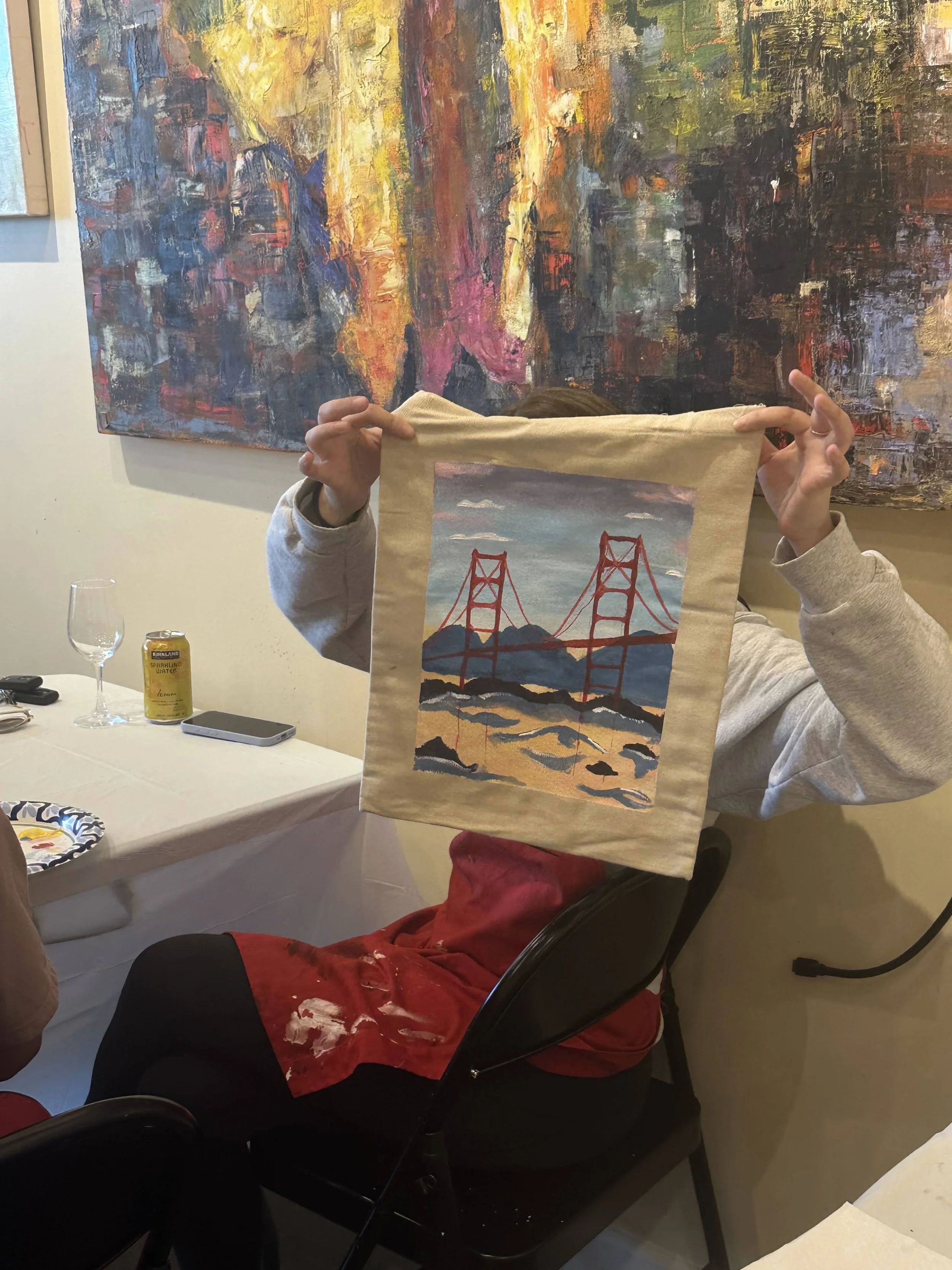 Person holding up a fabric with an embroidered or printed picture of the Golden Gate Bridge against a landscape.