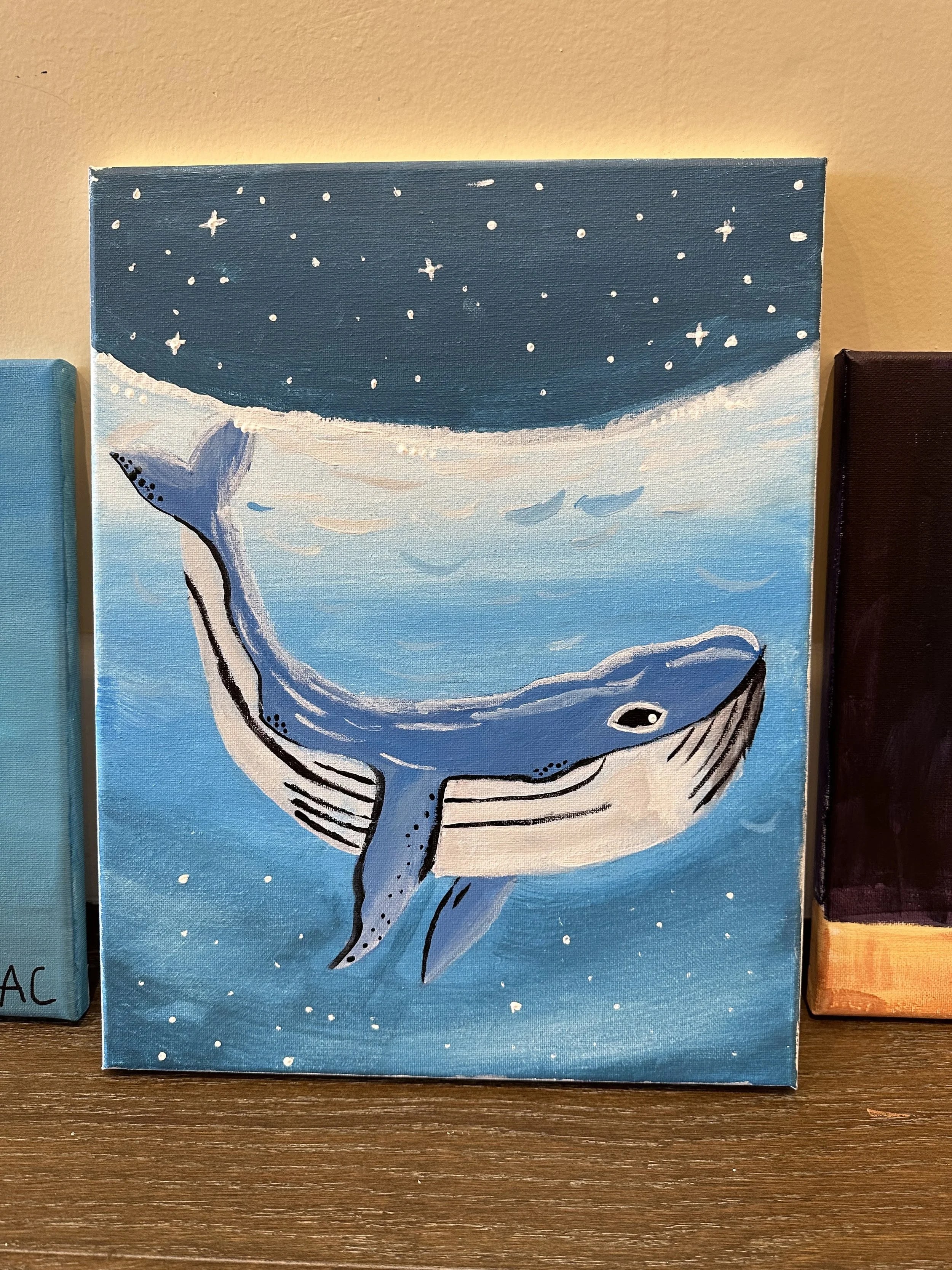 Painting of a whale swimming in the ocean with a starry night sky above.