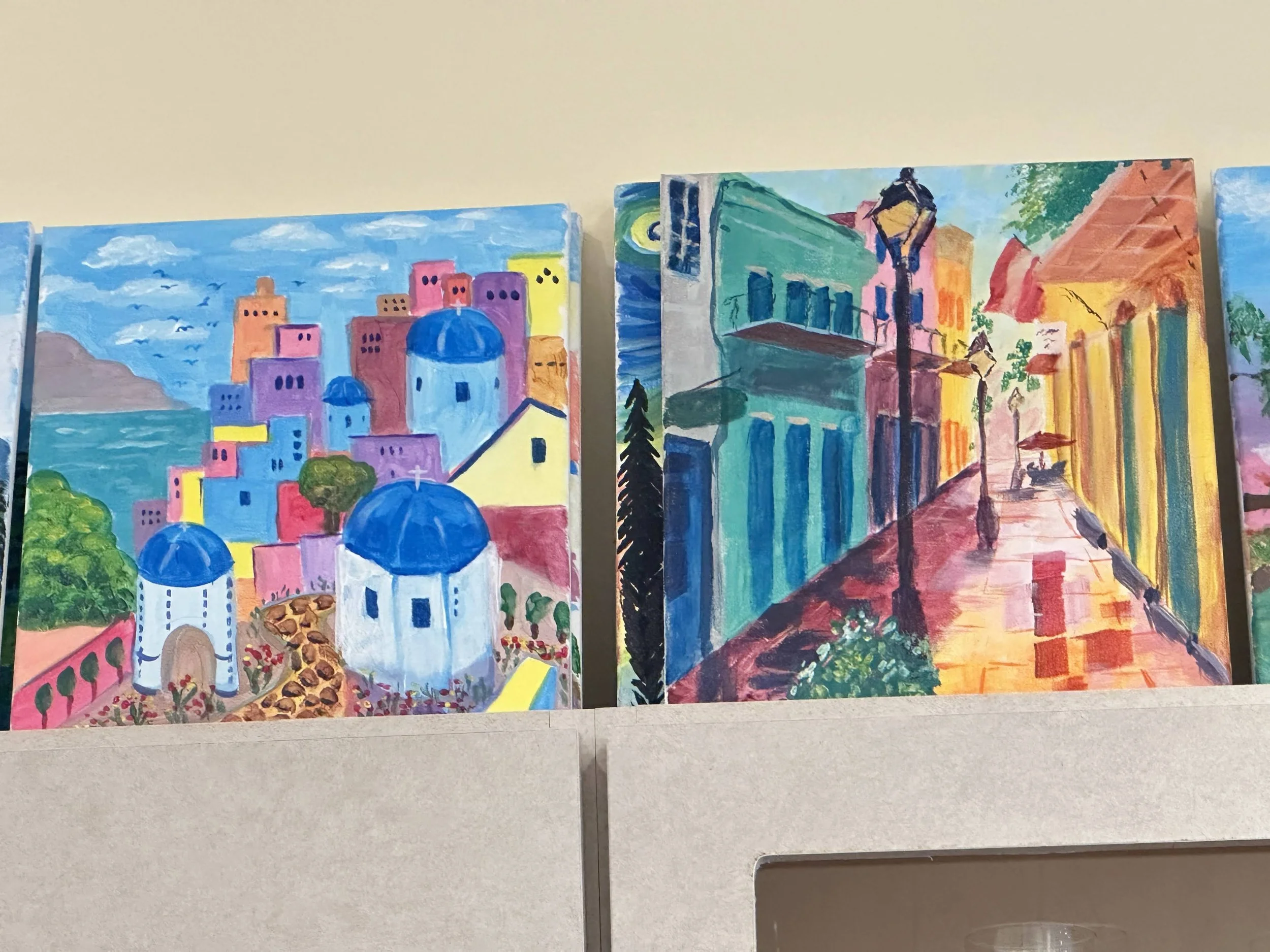 Colorful paintings of Mediterranean cityscapes with bright buildings, streets, and churches.