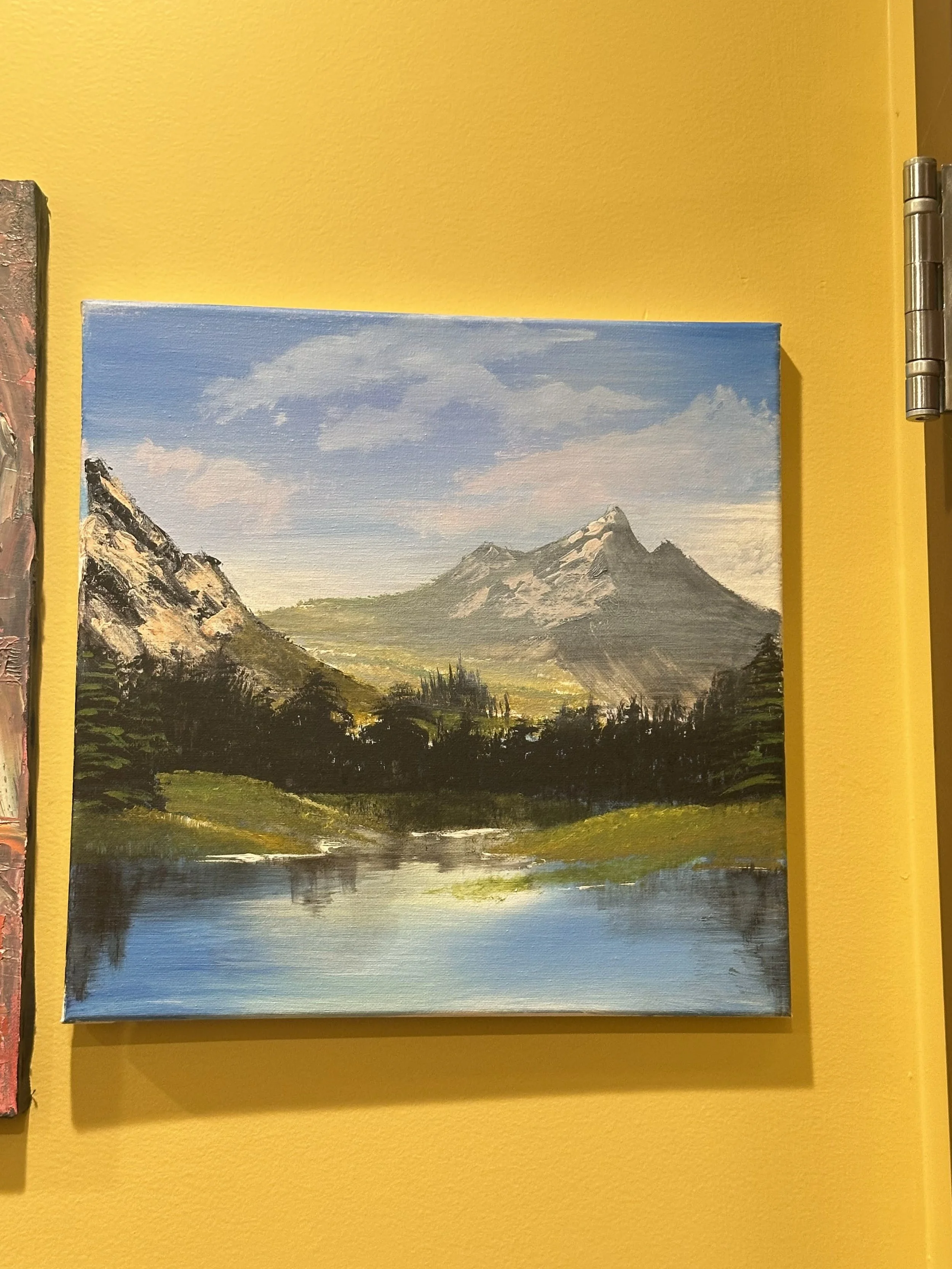 A landscape painting of mountains, trees, and a lake with a partly cloudy sky.