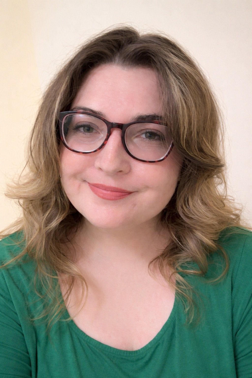 A woman with wavy, shoulder-length hair wearing glasses and a green top, smiling at the camera.