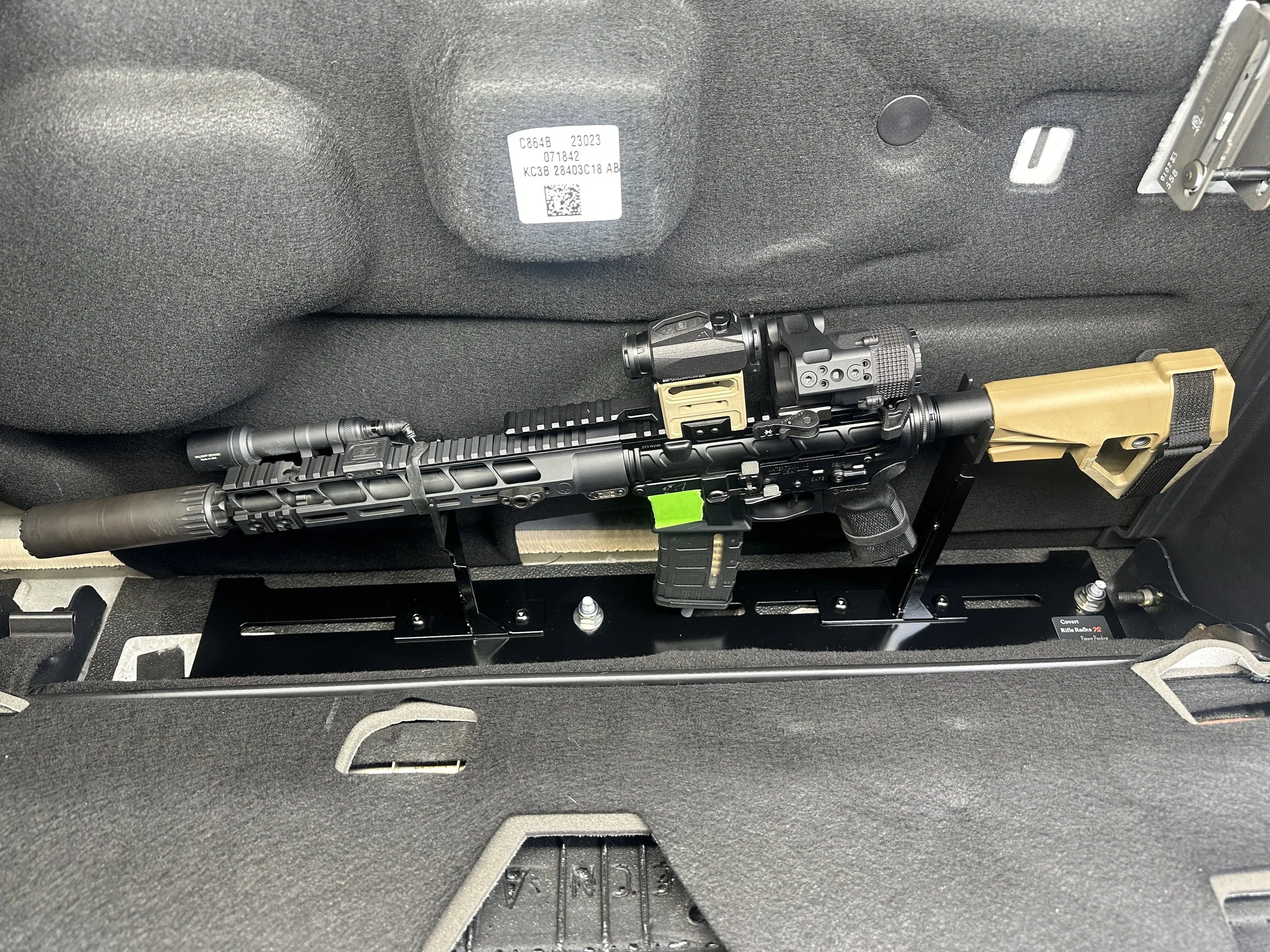 A firearm secured in a vehicle, with a scope and suppressor attached, mounted on a black platform.