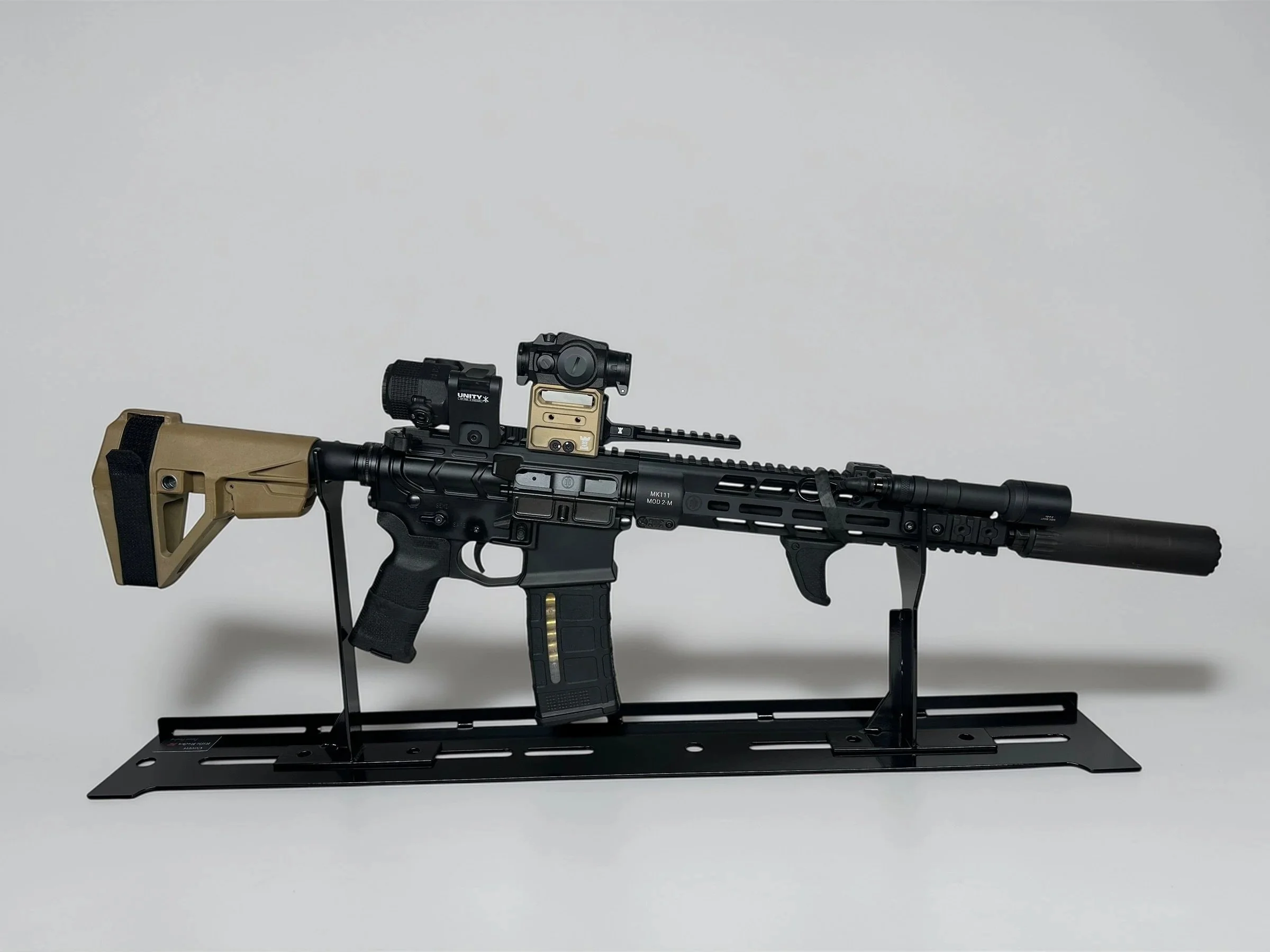 Modern tactical rifle with attachments displayed on a black stand against a white background.