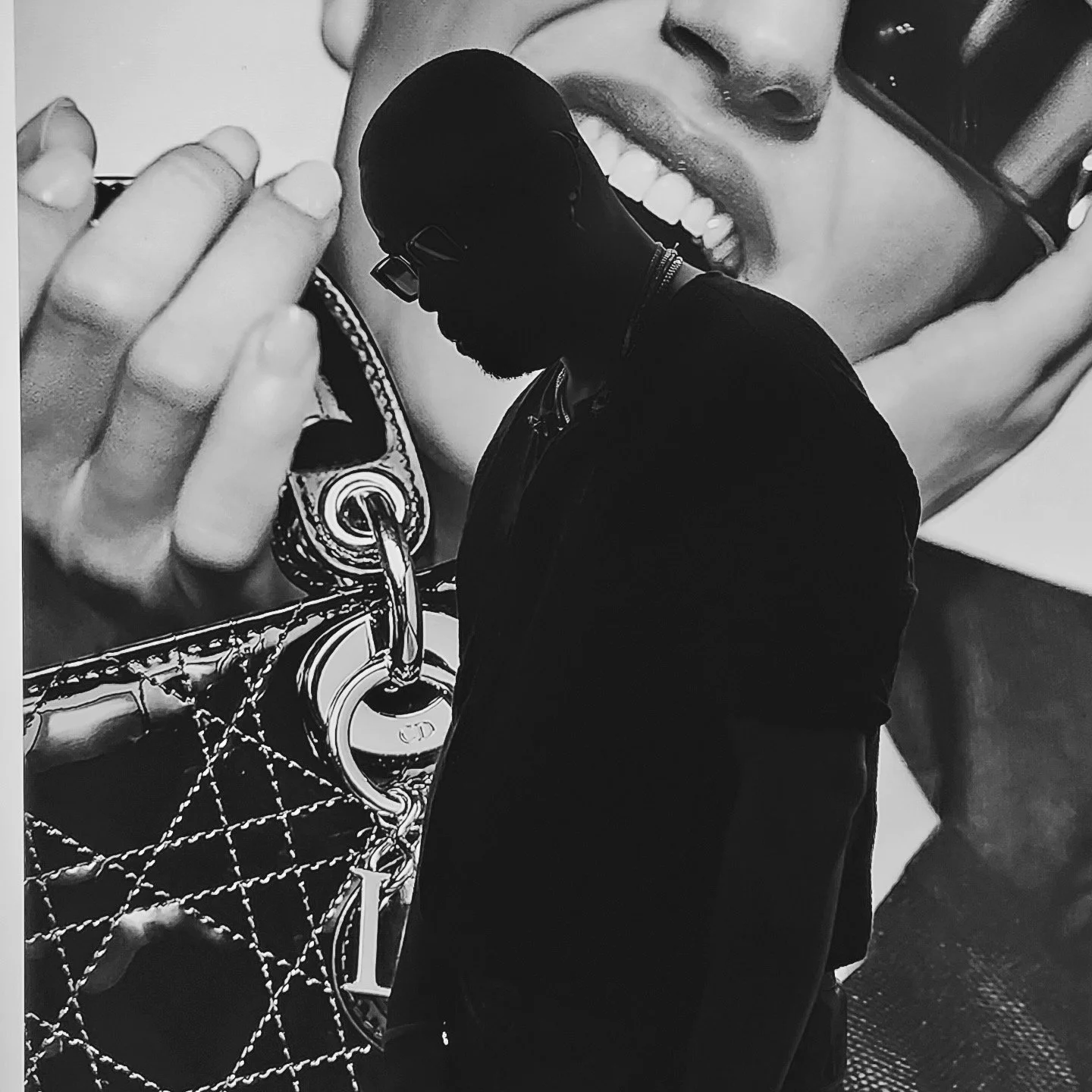 A black-and-white photo of a man in profile holding a quilted designer bag, with a large advertisement featuring a woman's face in the background.