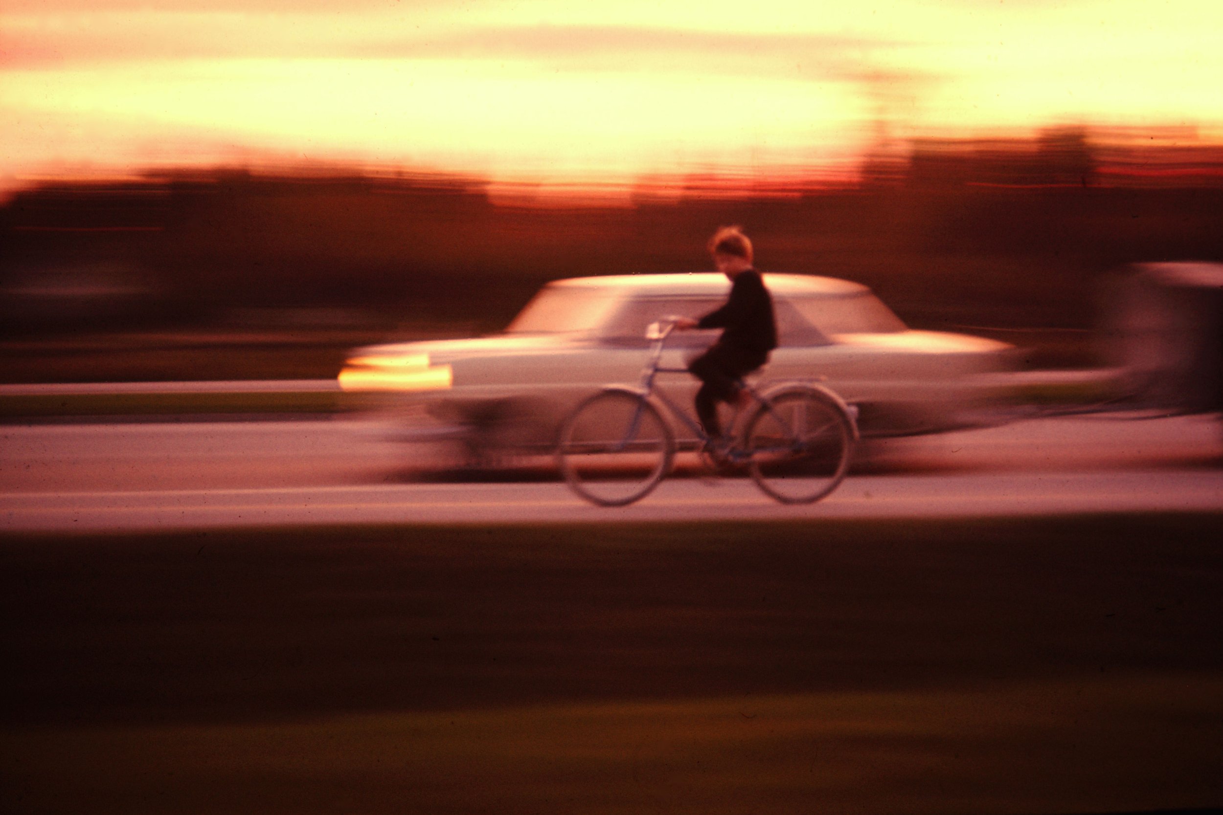 Skannad diabilder som visar en person som cyklar framför en bil.