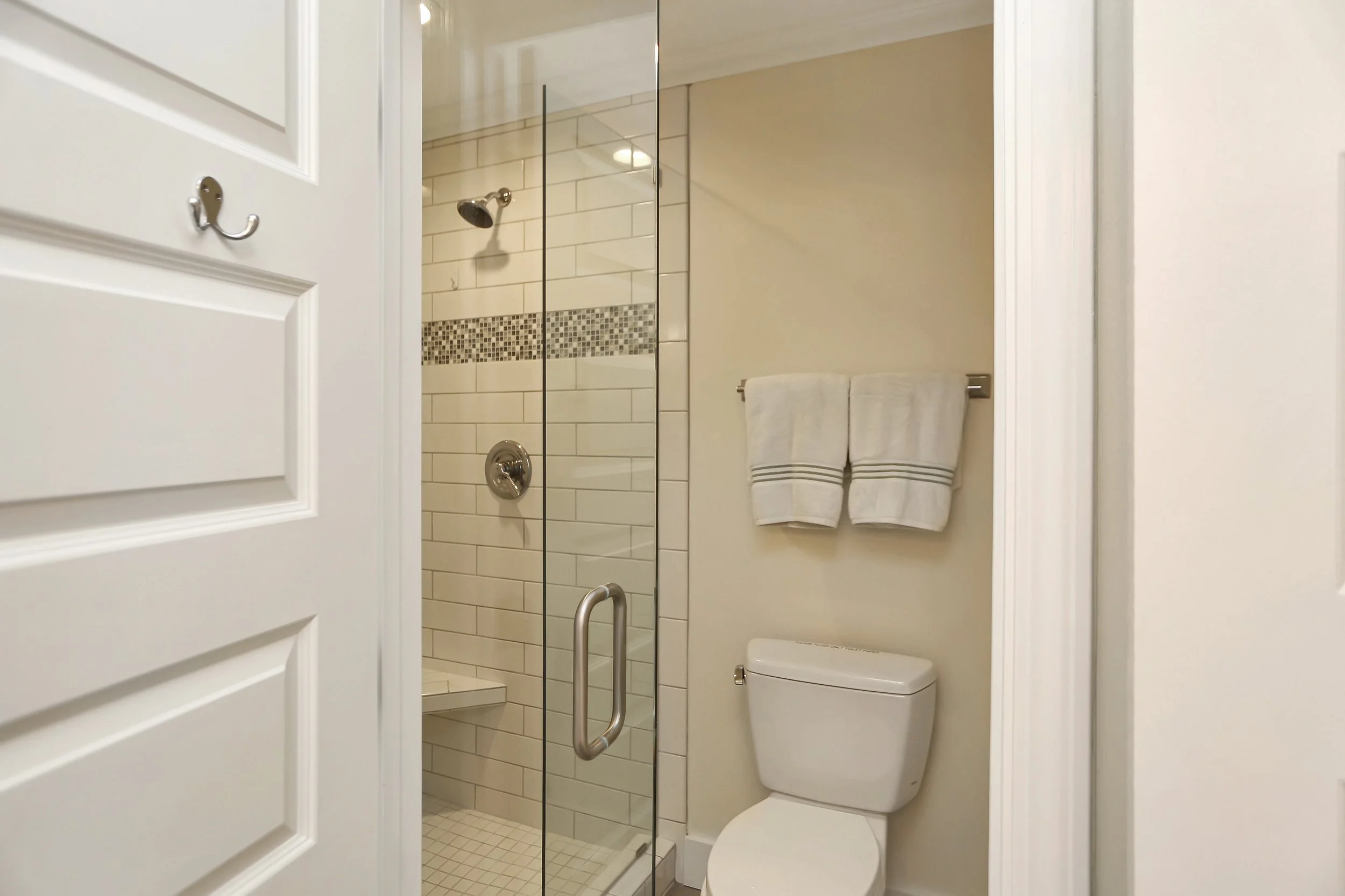 Bathroom with a glass shower enclosure, white subway tile, a mosaic border, a towel rack with two white towels, and a toilet.