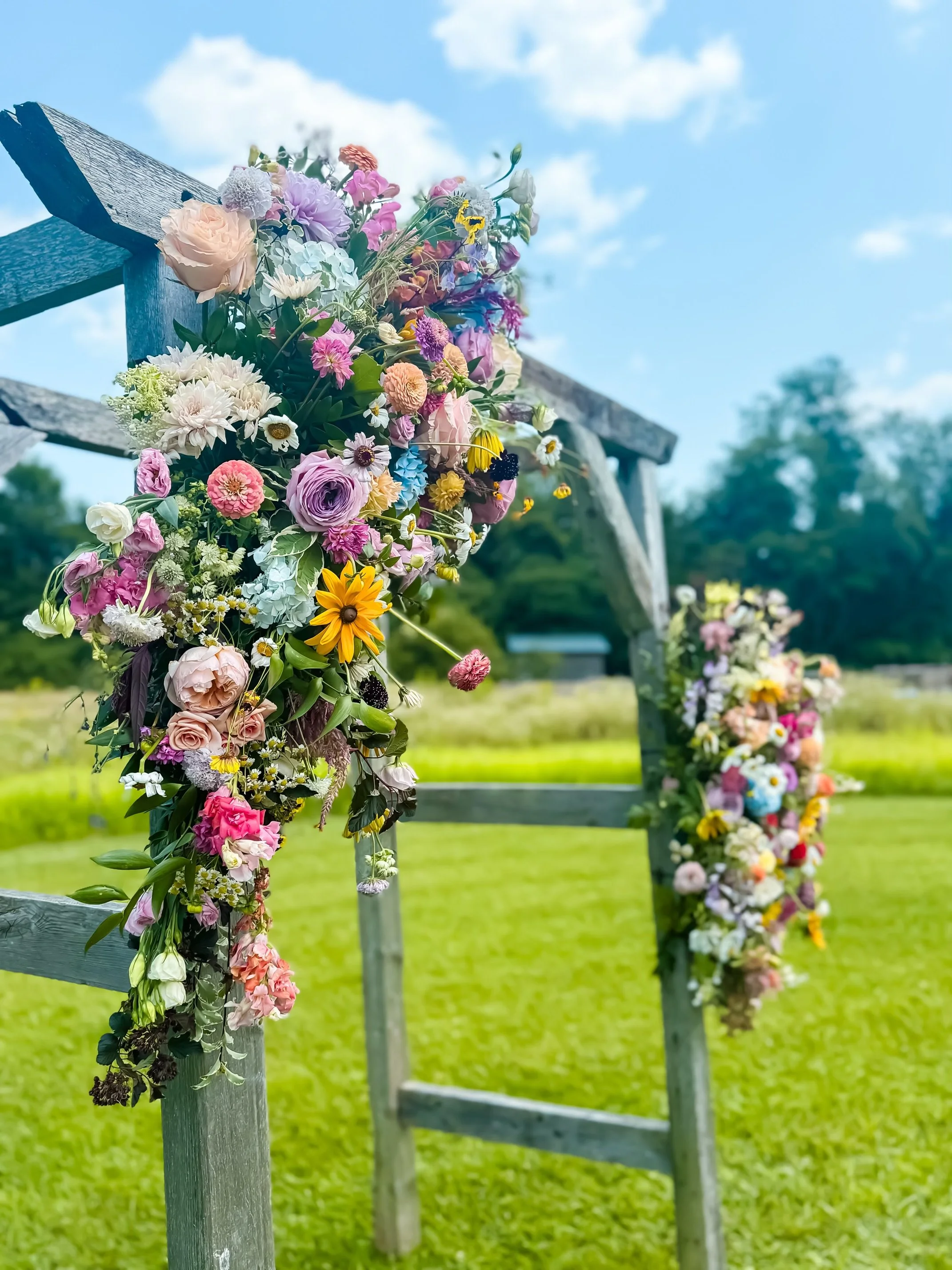 Colorful flower arrangements attached to wooden railings outdoors on a sunny day with a blue sky and white clouds.