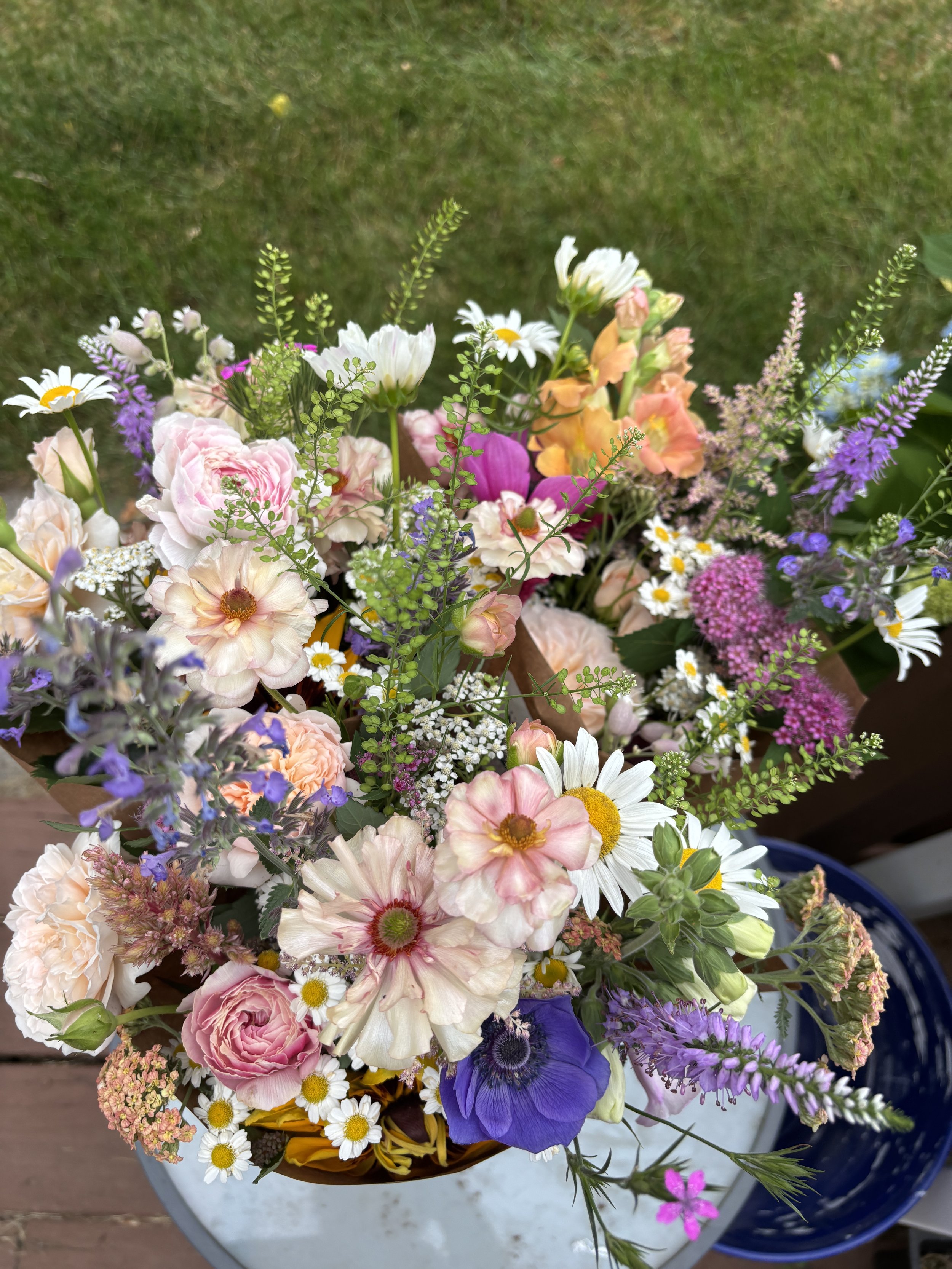 A colorful bouquet of various flowers including daisies, roses, and lavender in a white and blue vase on a wooden surface.