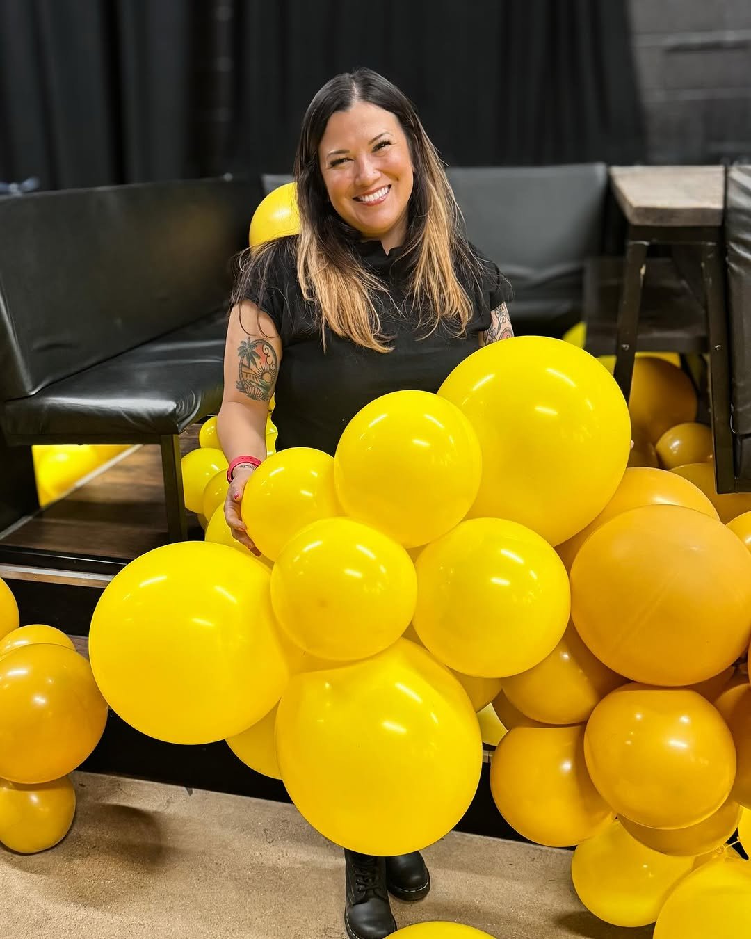 Woman smiling sitting among yellow balloons in a room with black furniture