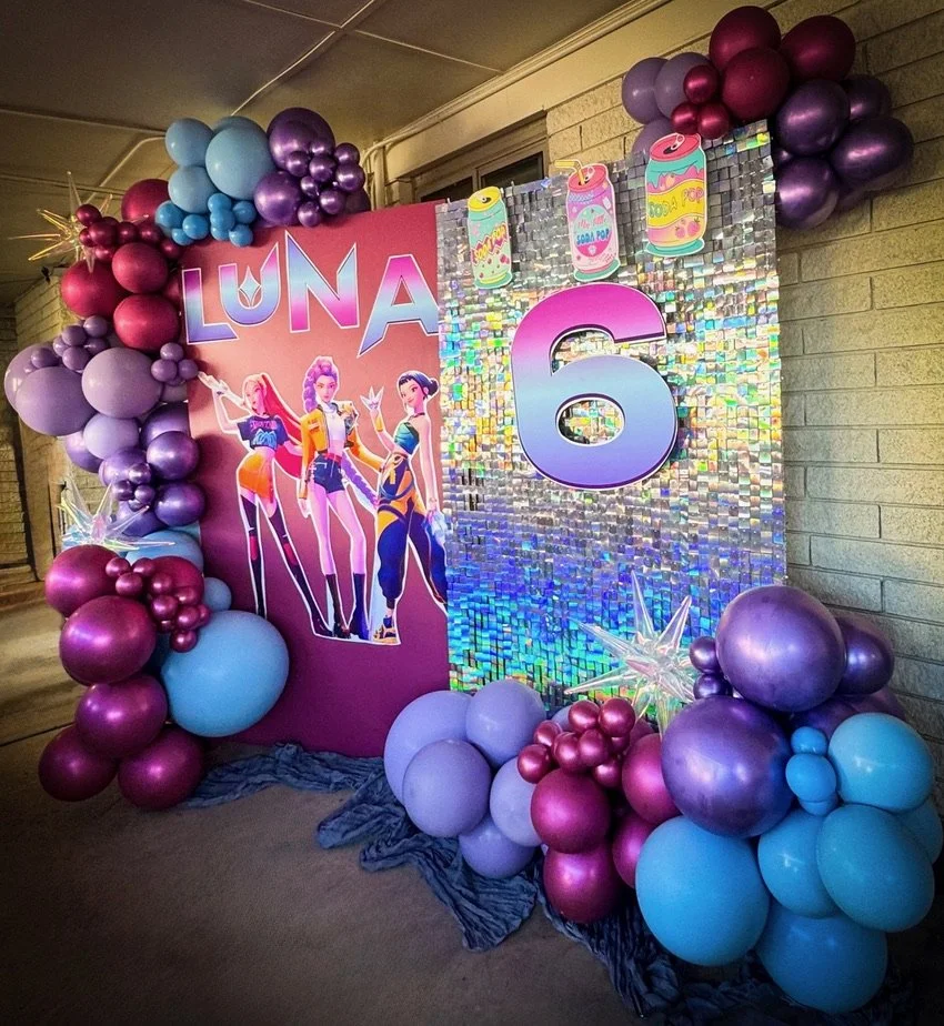Decorated birthday backdrop with balloons in shades of purple, pink, and blue for a girl named Luna's 6th birthday, featuring a holographic panel with a large number 6 and illustrations of three animated girls.