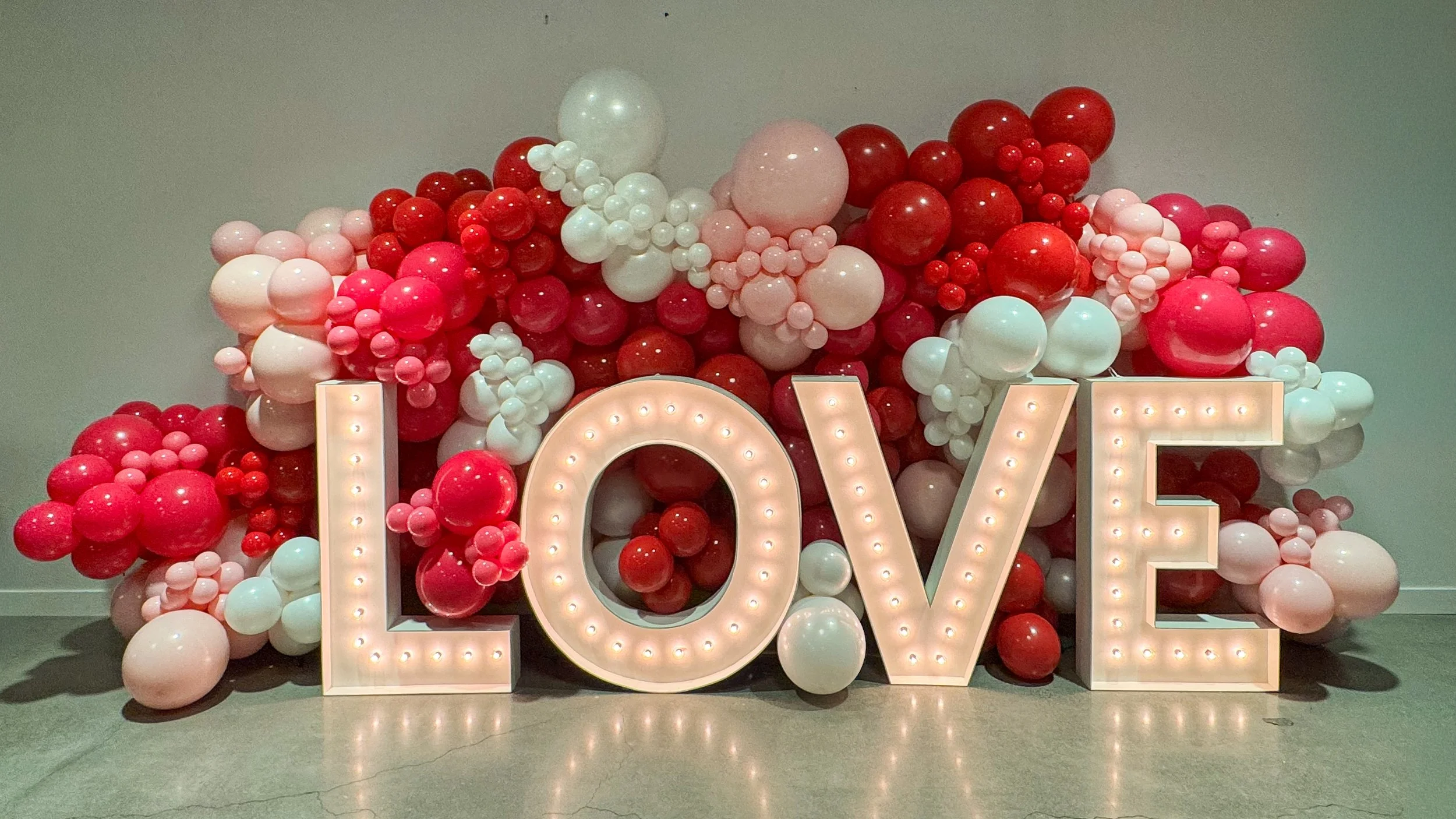 Decorative display with pink, red, and white balloons arranged around a large illuminated sign spelling 'LOVE'.