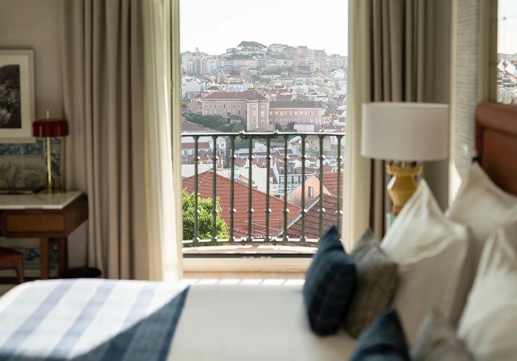 A hotel room with a bed near a window showing a cityscape with buildings and red-tiled roofs.