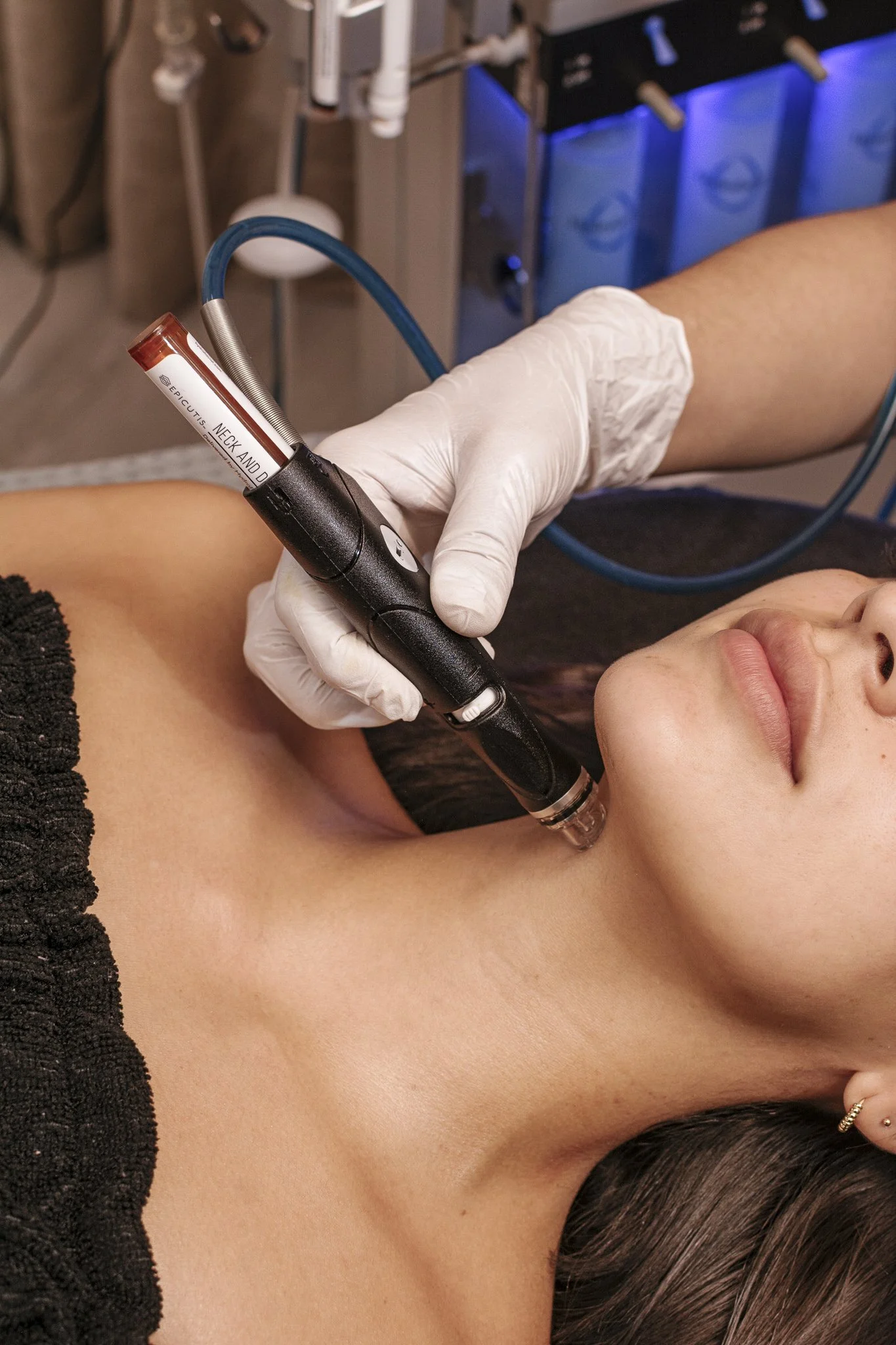 Una persona recibe un procedimiento médico en la parte del cuello con un dispositivo que parece un láser o una máquina de inyección, en un entorno clínico.
