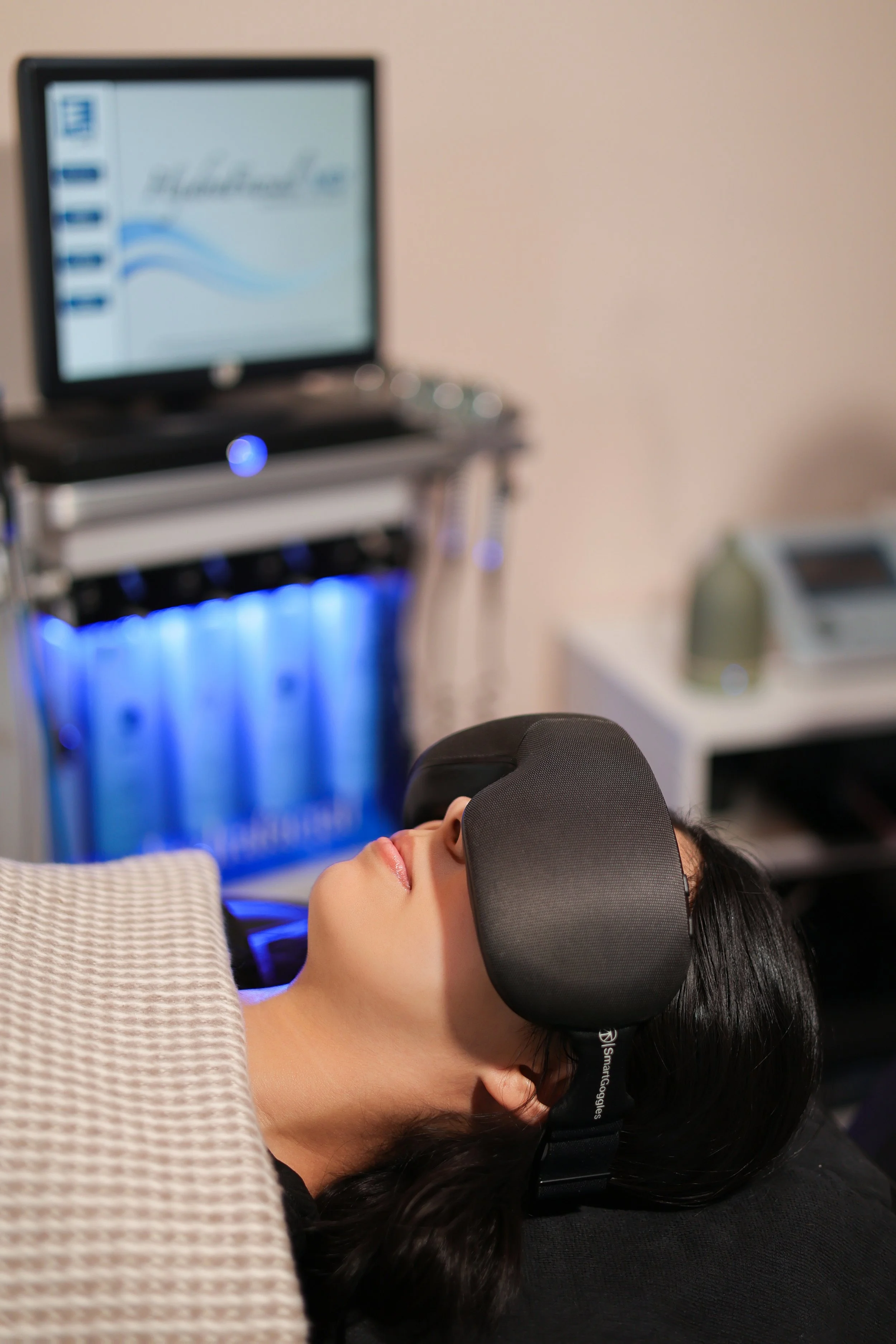 Persona acostada usando un visor de realidad virtual en un entorno de oficina o clínica, con monitor y equipo médico o tecnológico en el fondo.