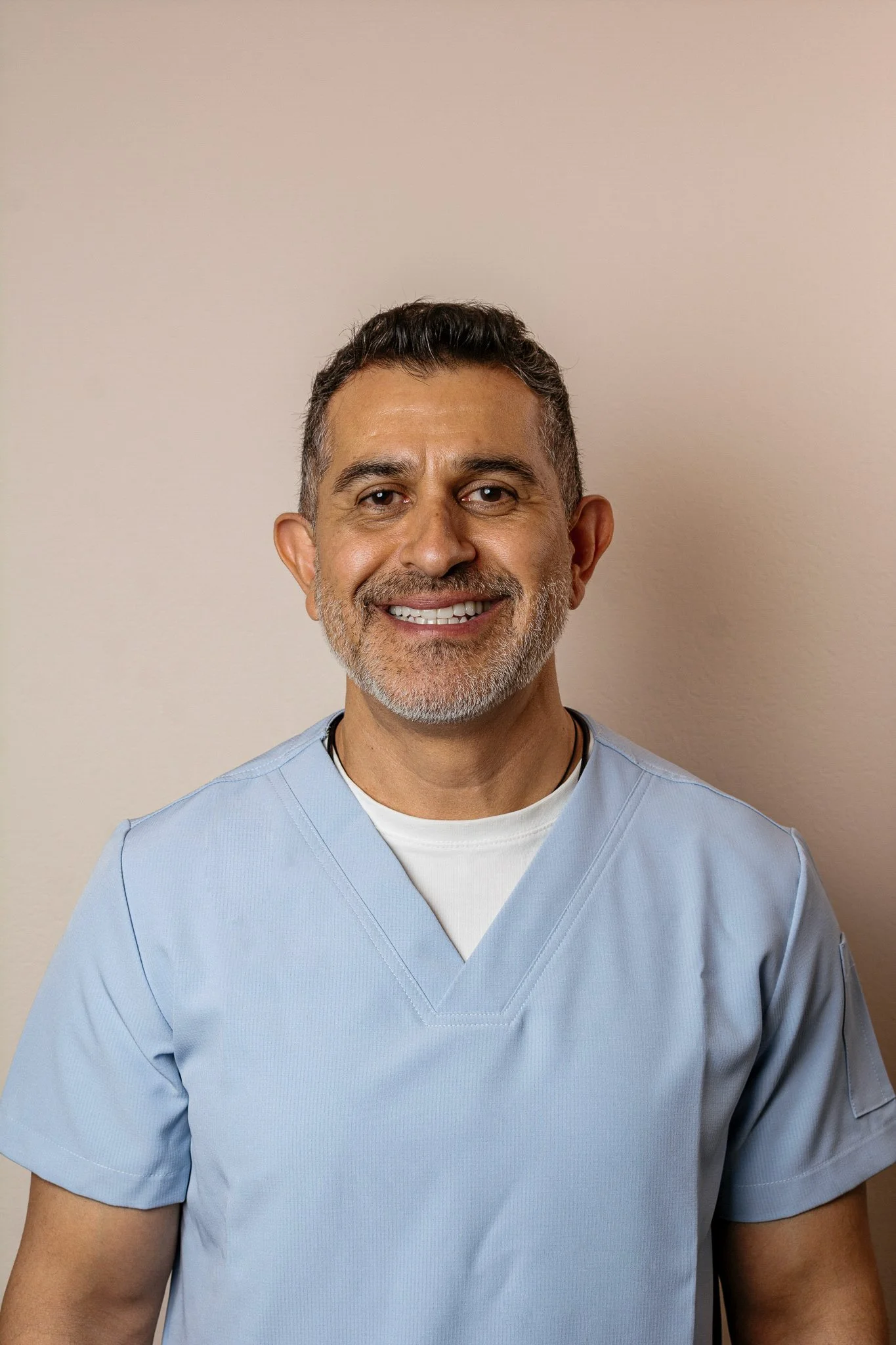 Hombre con barba con uniforme de enfermero sonriendo en un fondo neutral.