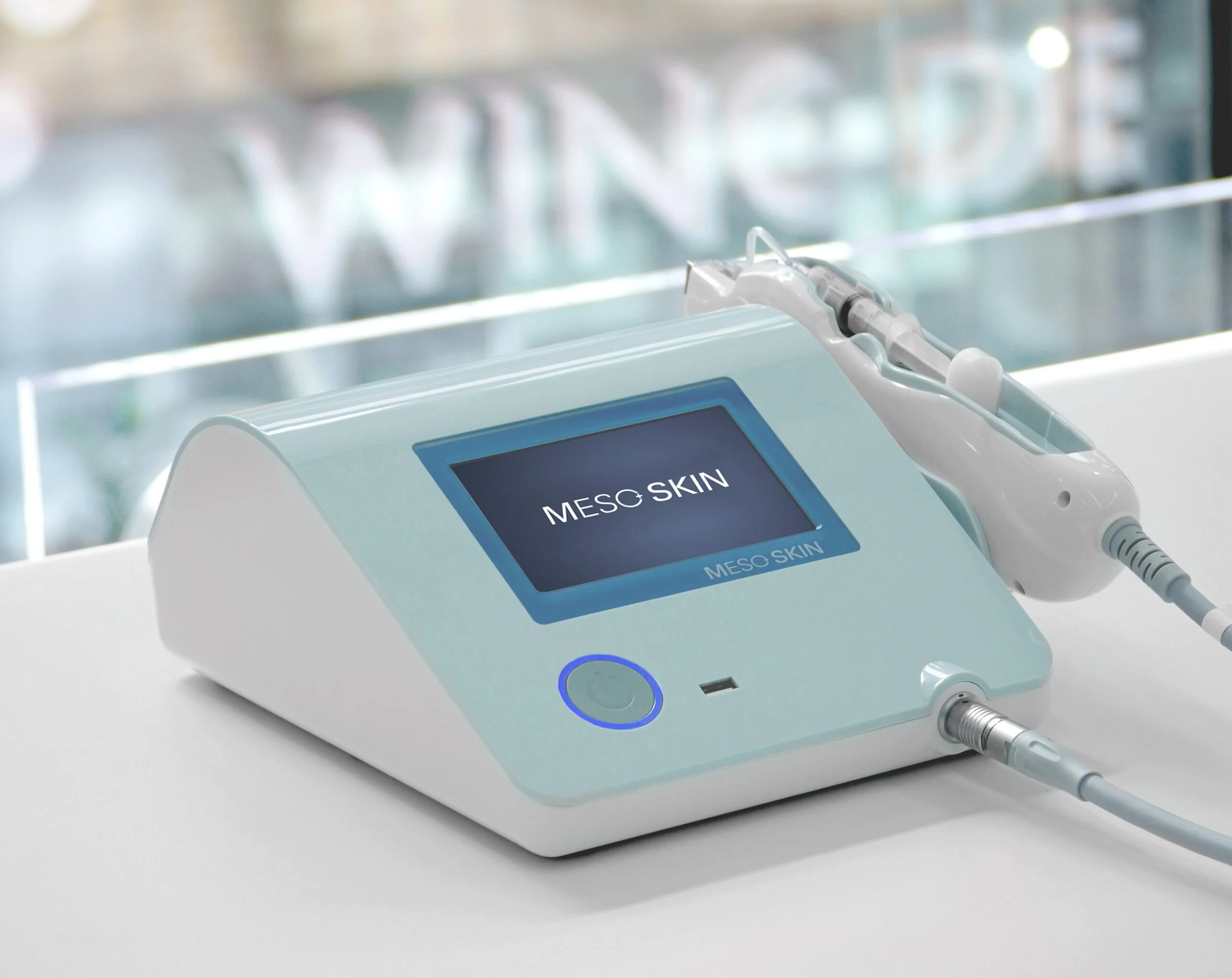 Dispositivo médico con pantalla digital que dice 'MESO SKIN' y tiene un aplicador conectado y una interfaz en forma de botón circular iluminado en azul.