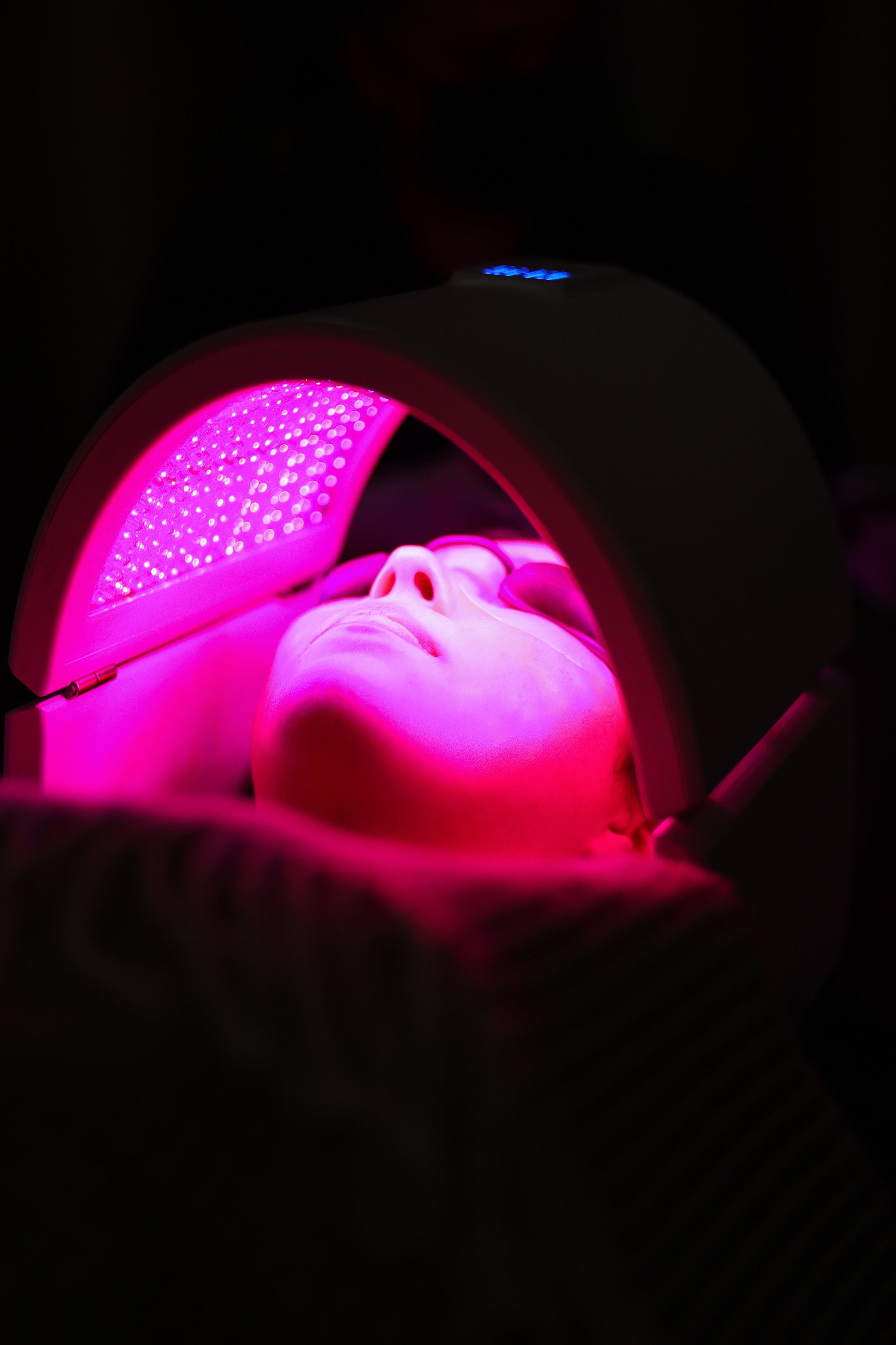 Una persona recibiendo terapia de luz LED rosa en la cara con una máquina de fototerapia.