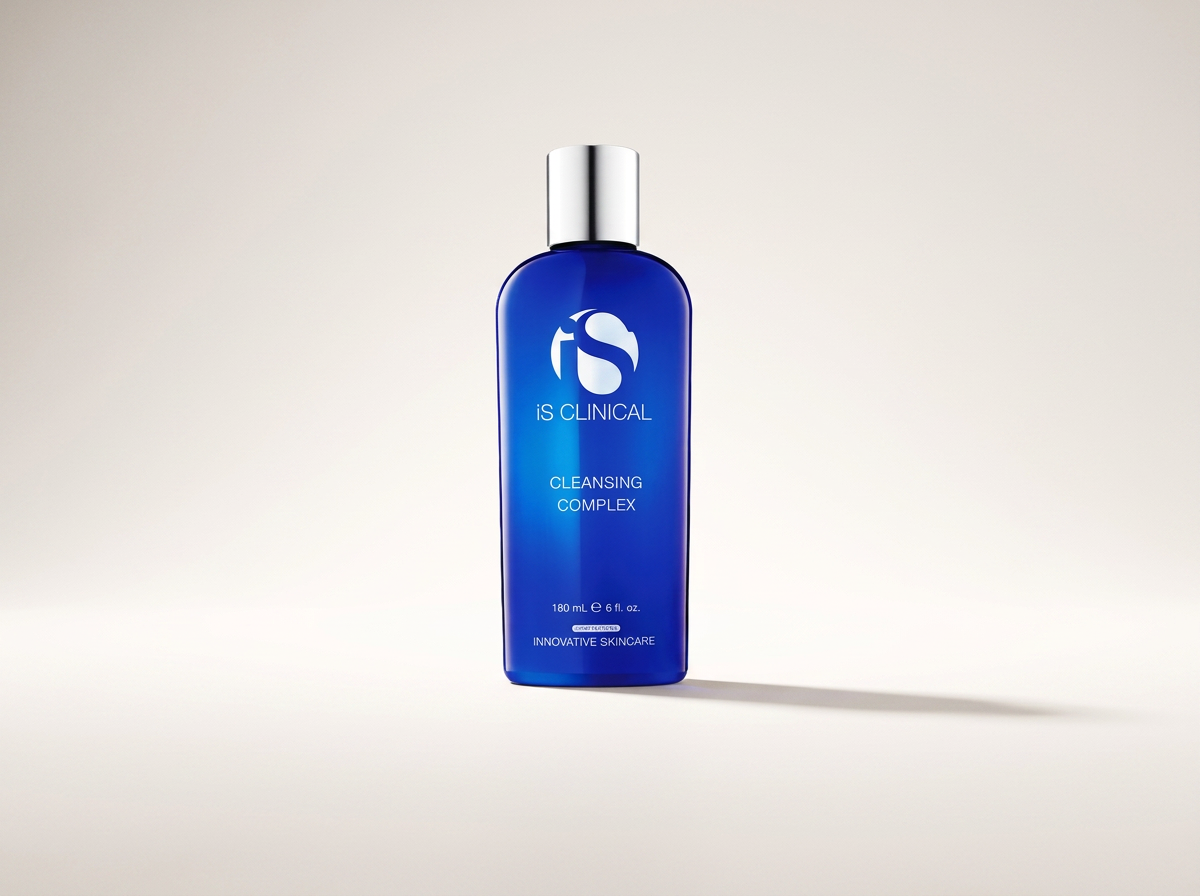 Botella azul de producto iS Clinical Cleansing Complex con tapa plateada, en fondo claro y sombra