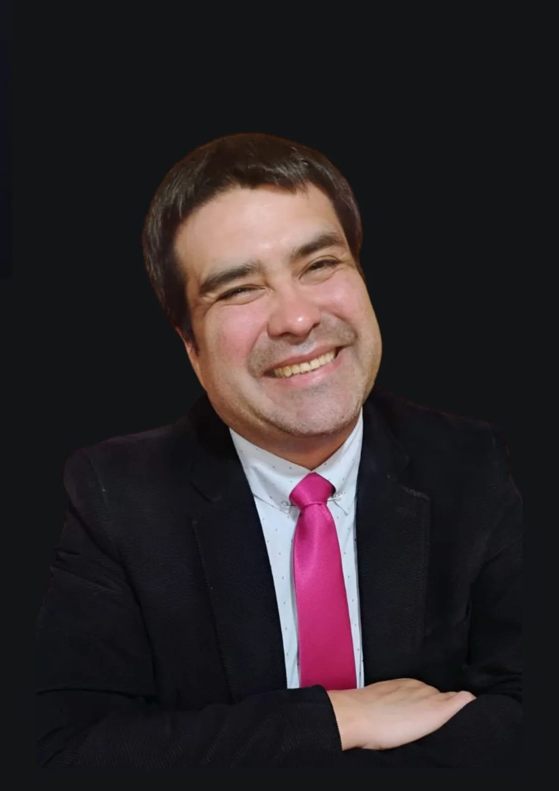 Hombre sonriendo con cabello oscuro, usando saco negro, camisa blanca con puntos y corbata rosa, con fondo negro.