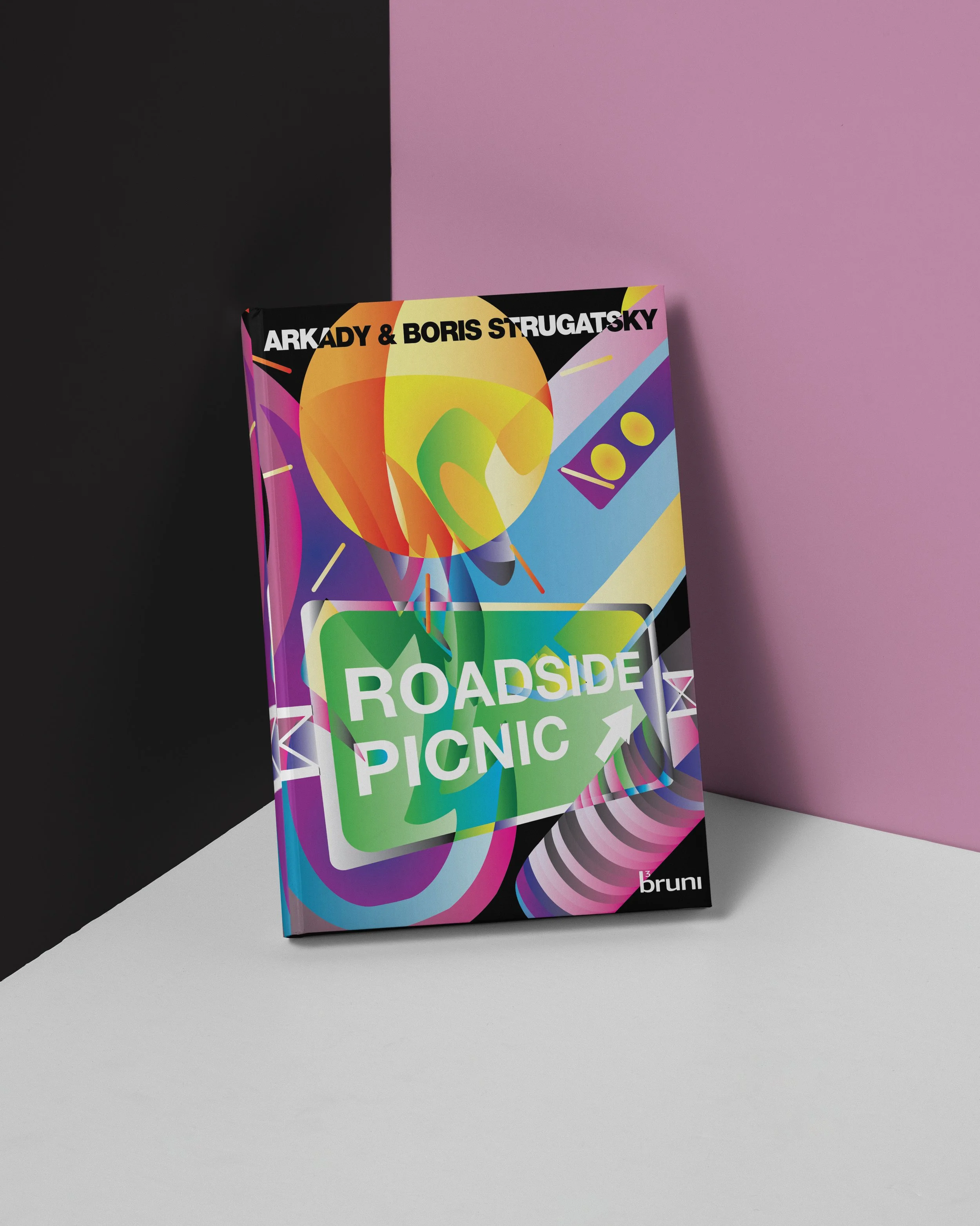 A colorful book cover titled 'Roadside Picnic' by Arkady & Boris Strugatsky, with vibrant abstract artwork, placed on a flat surface against a split-colored background of black, pink, and white.