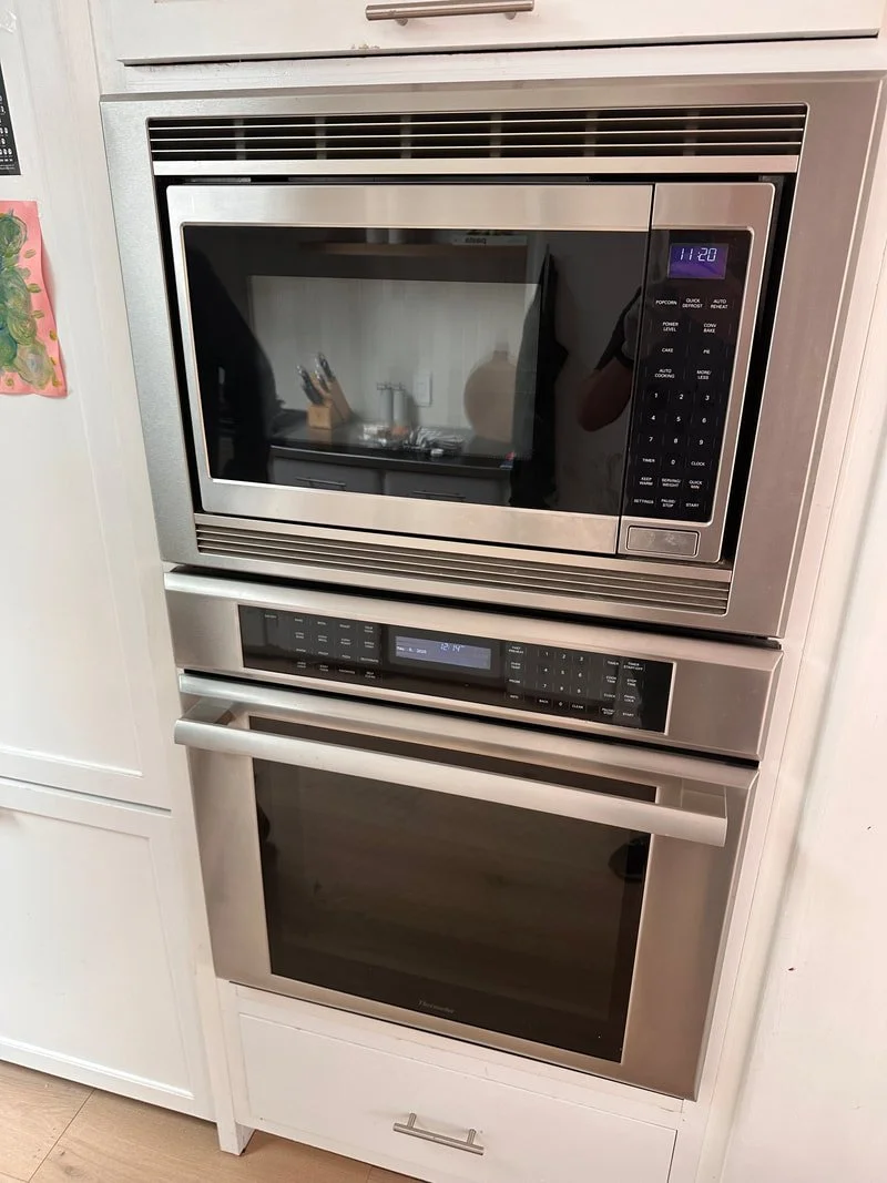 Stainless steel microwave and oven built into white kitchen cabinetry.