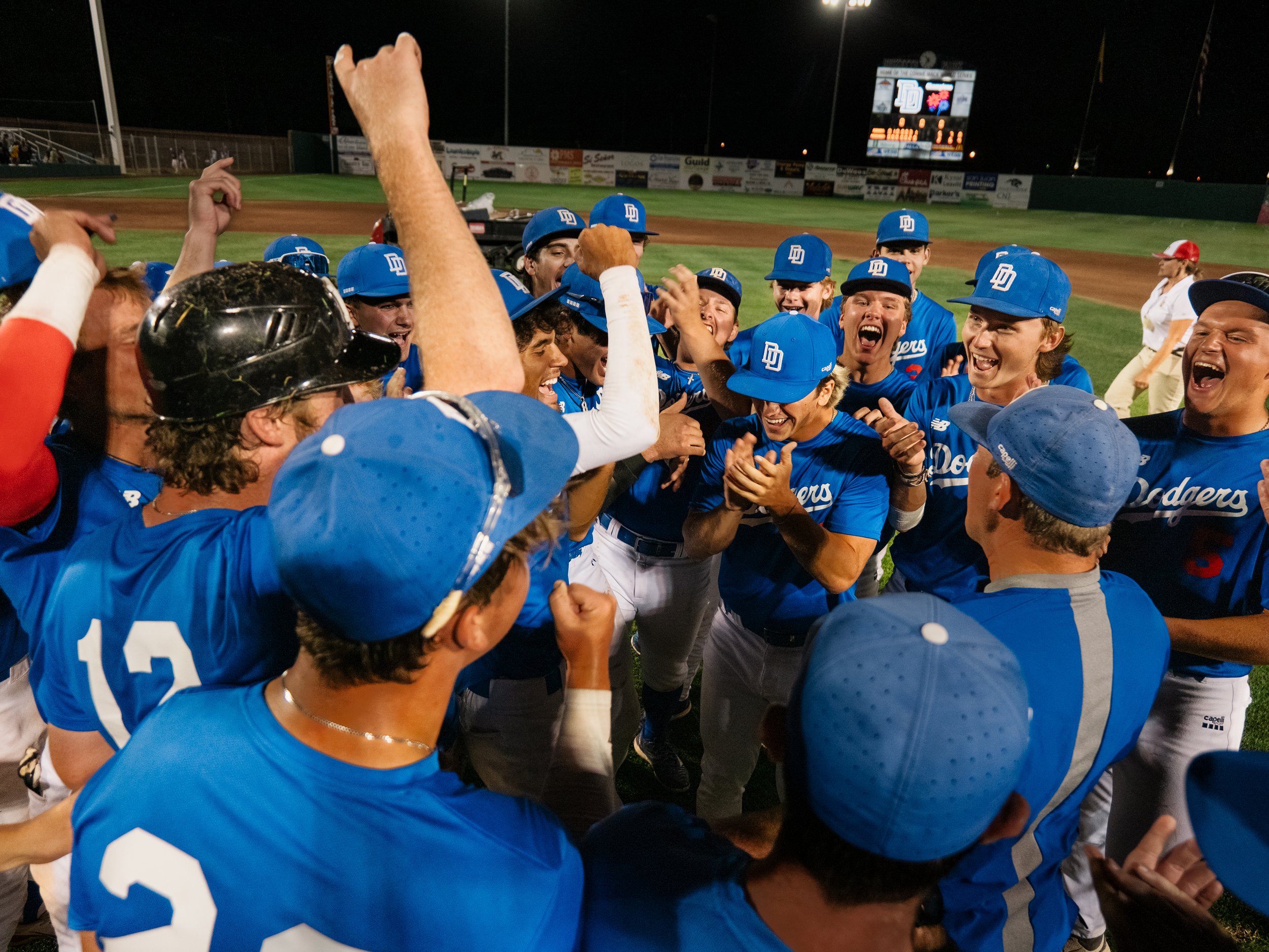 A group of baseball players in blue uniforms celebrating together on a field at night.
