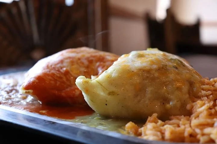 Two stuffed peppers with melted cheese on a plate, served with rice.