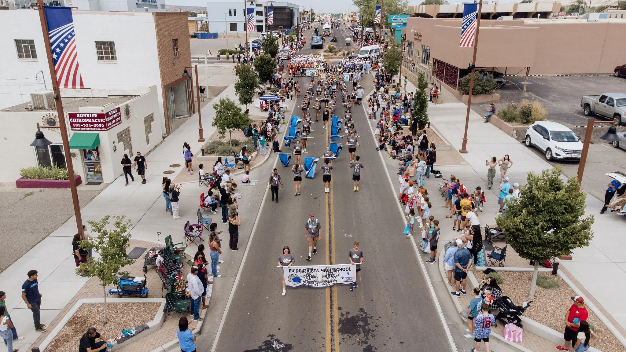 A parade on a city street with people lining the sidewalks and participating in the event, carrying banners, and wearing casual clothing.