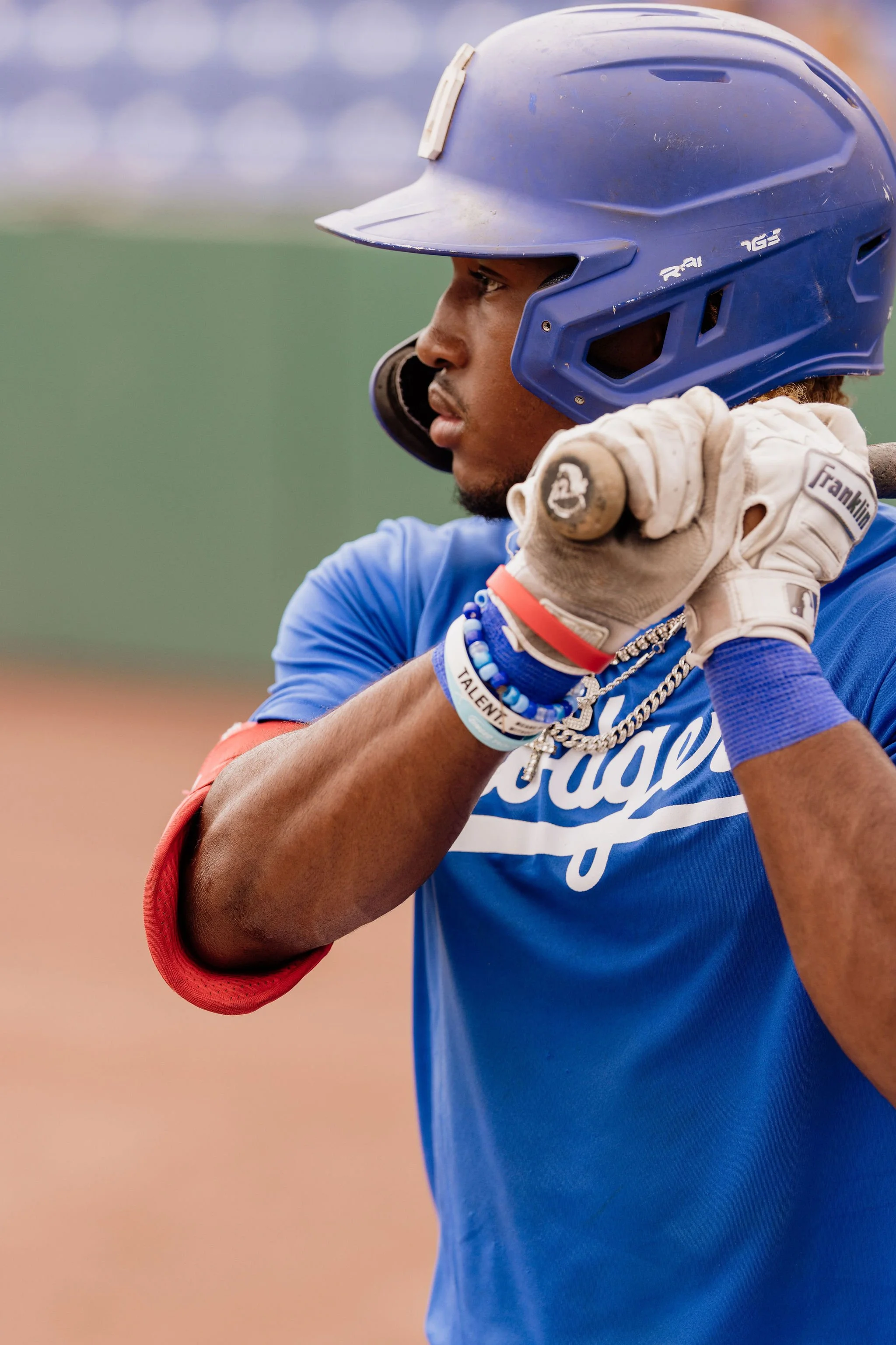 A baseball player wearing a royal blue helmet and matching blue jersey, adjusting his helmet with one hand, with a tan glove tucked under his arm.