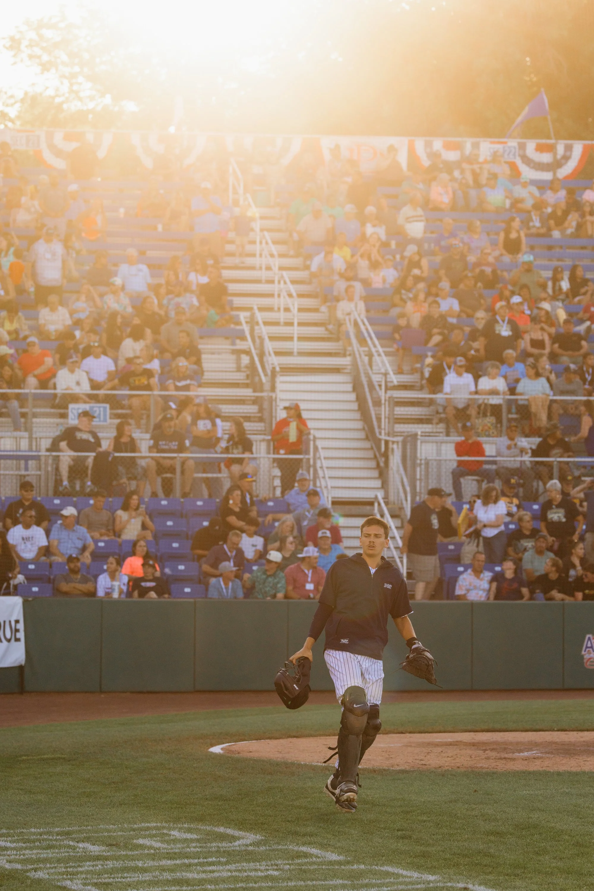 A baseball player walking off the field, holding a baseball glove and helmet, with a crowd of spectators seated in the bleachers in the background.