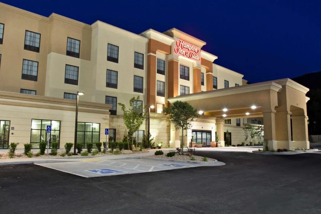 Hampton Inn & Suites hotel at night with parking lot, trees, and handicapped parking spaces in the foreground.