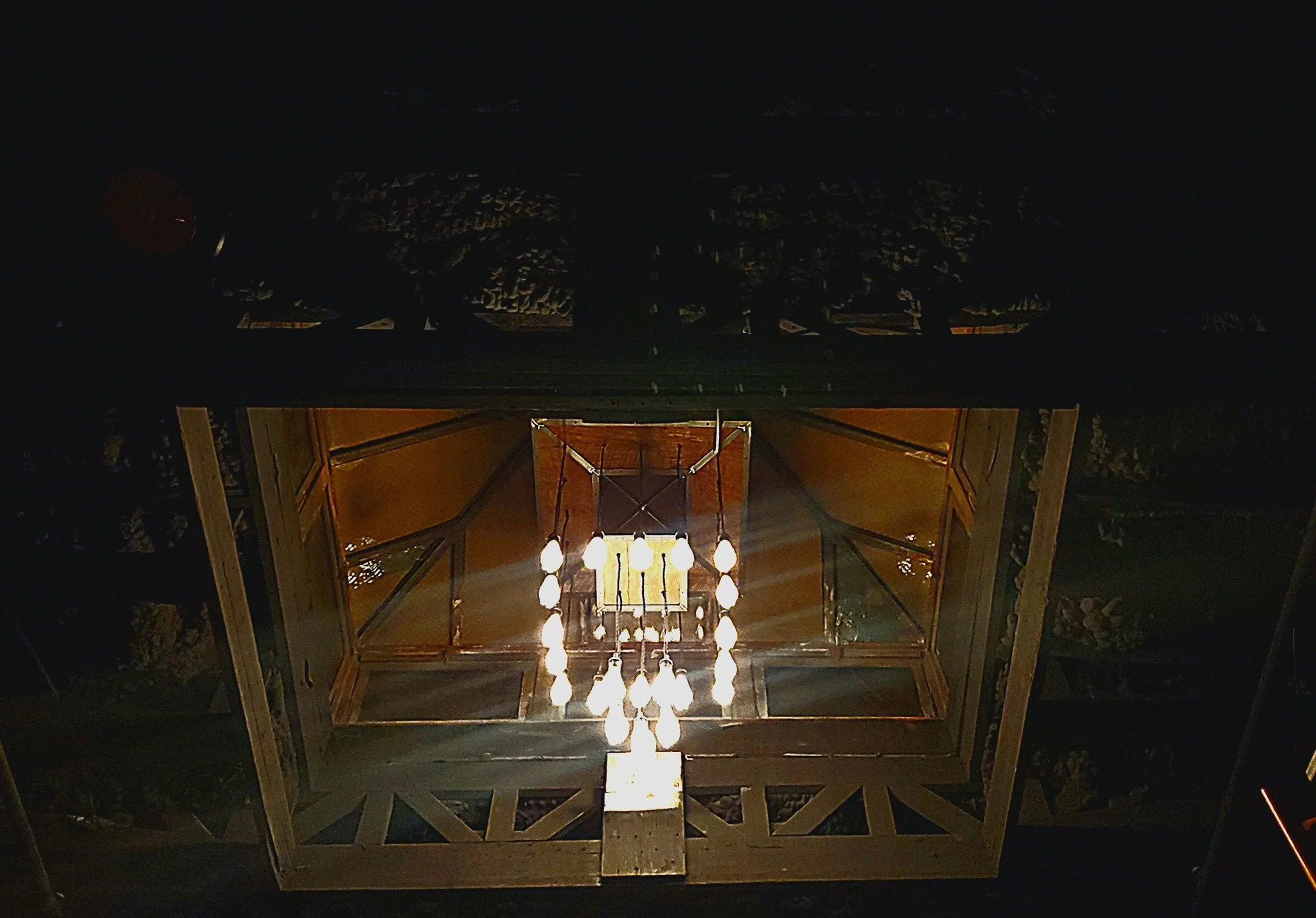 From below view of a chandelier with multiple bulbs illuminating a glass ceiling in a stairwell or atrium of a building.
