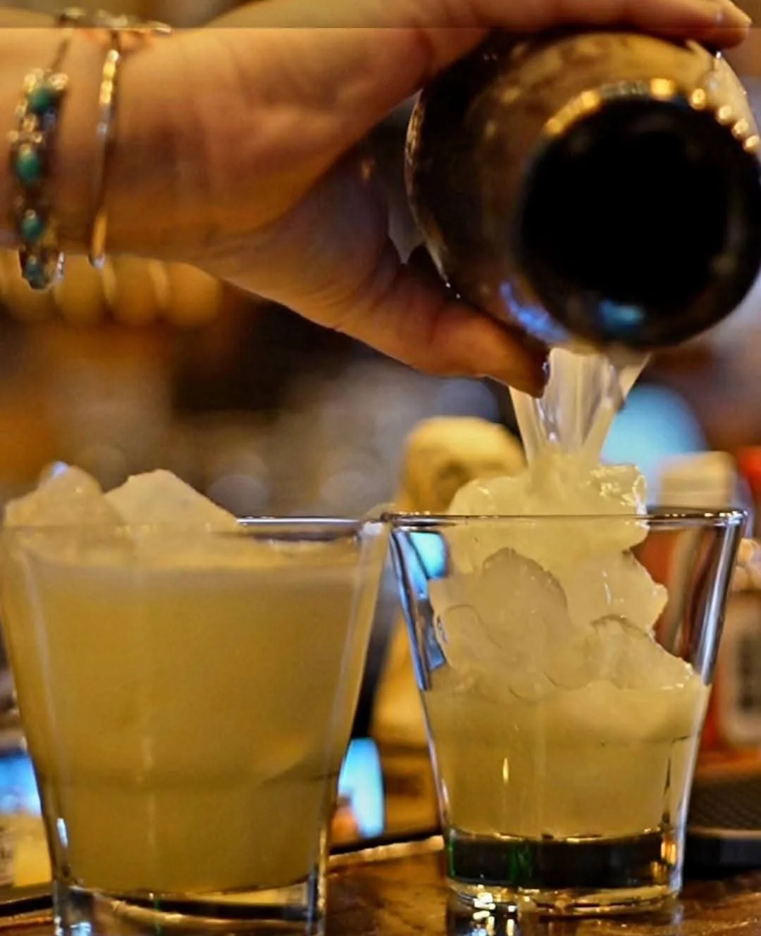 A hand pouring a dark beverage into a glass filled with ice cubes