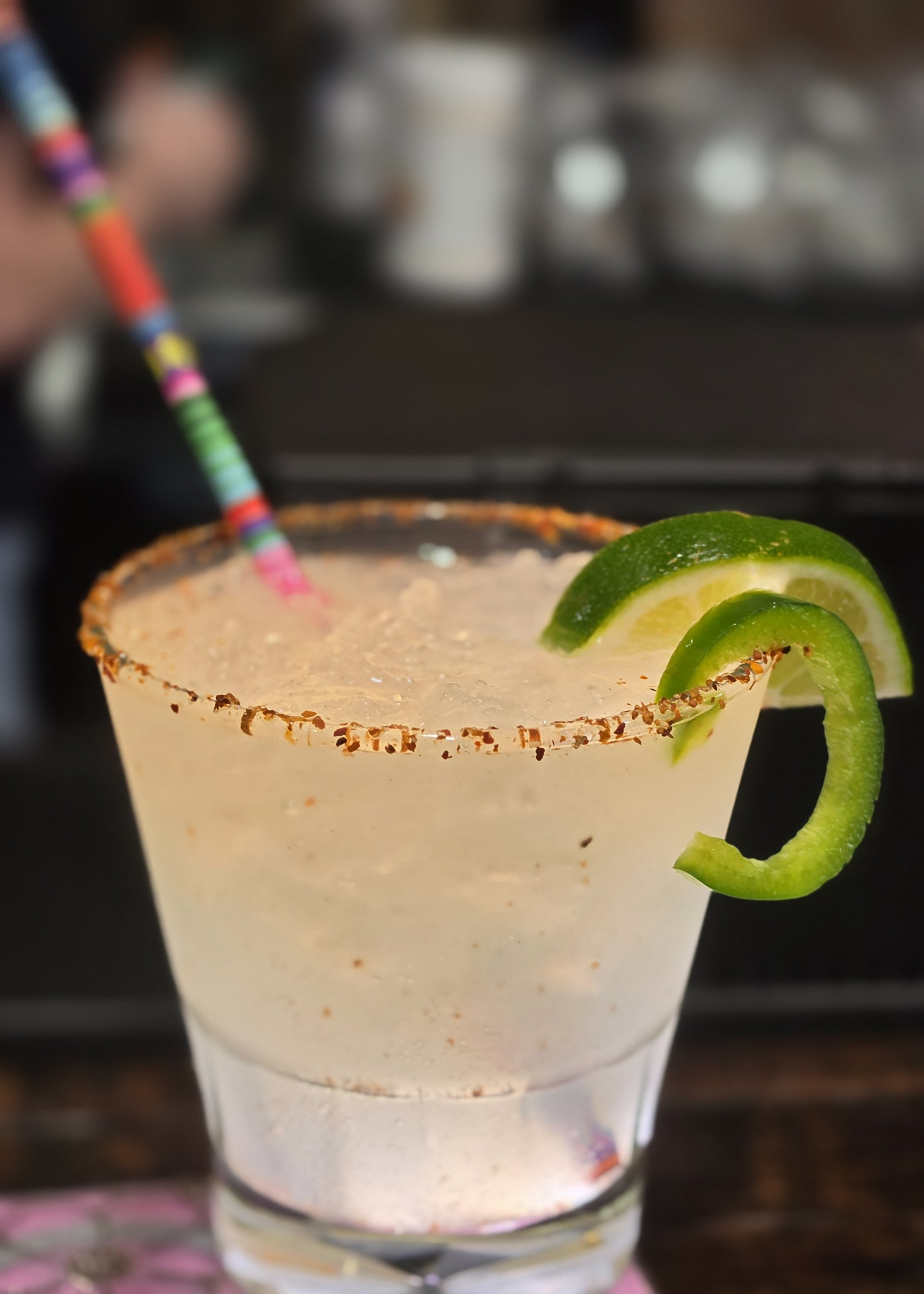 A close-up of a cocktail glass with salted rim, garnished with lime slices, and a colorful striped straw.