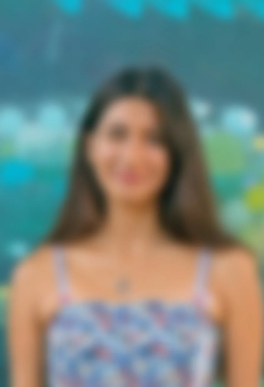 Blurry image of a woman with long dark hair wearing a sleeveless dress, standing outdoors with a colorful background.