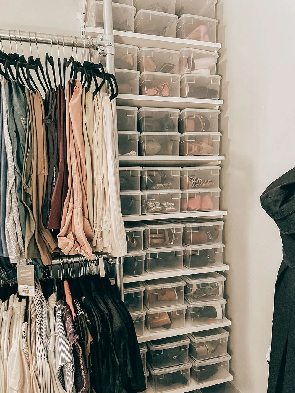 Closet with hanging clothes on the left and clear plastic storage bins on shelves on the right filled with shoes and accessories.