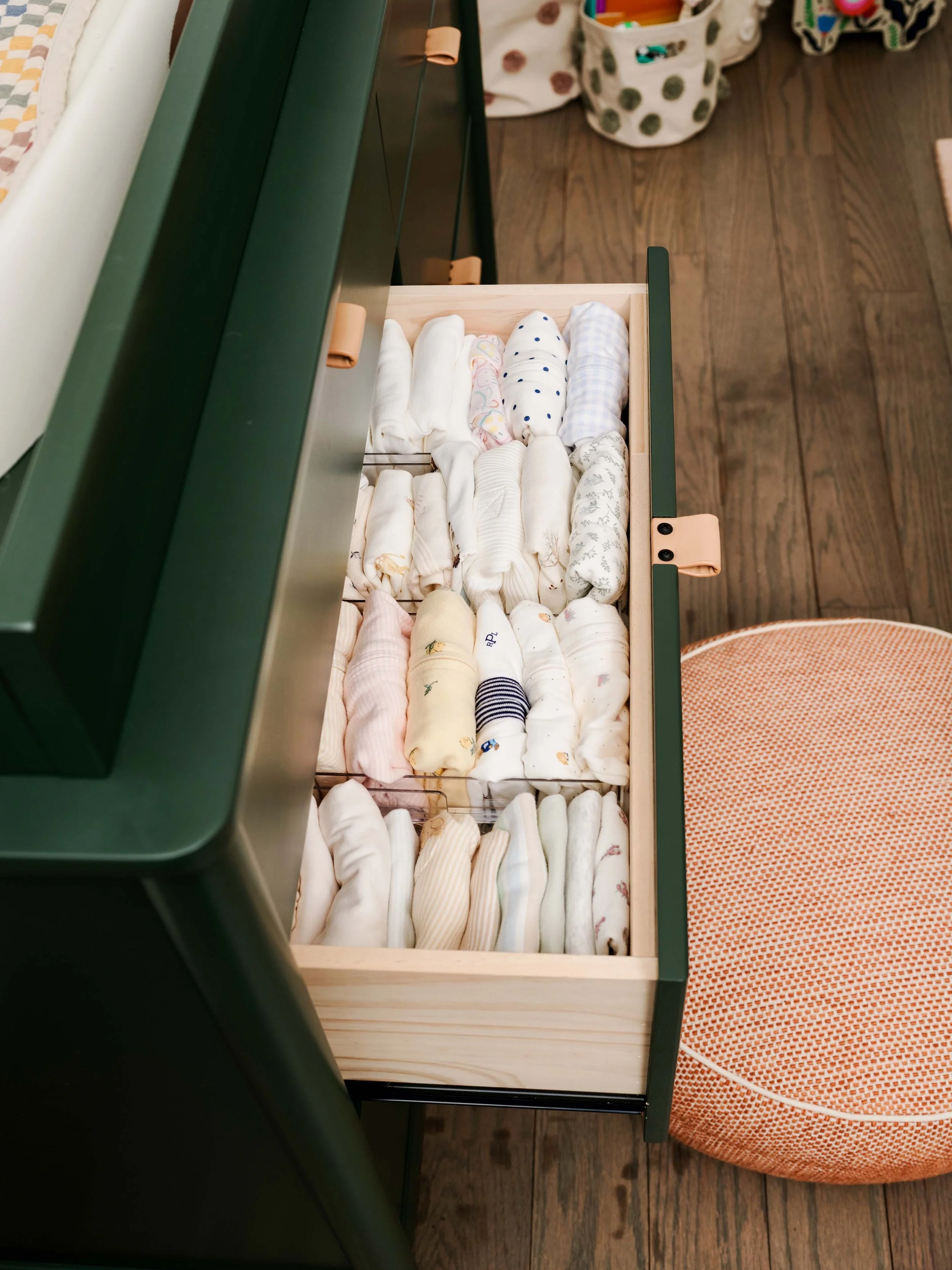 Open drawer filled with various rolled-up baby socks and cloth diapers, with a polka dot basket and an orange seat cushion nearby.