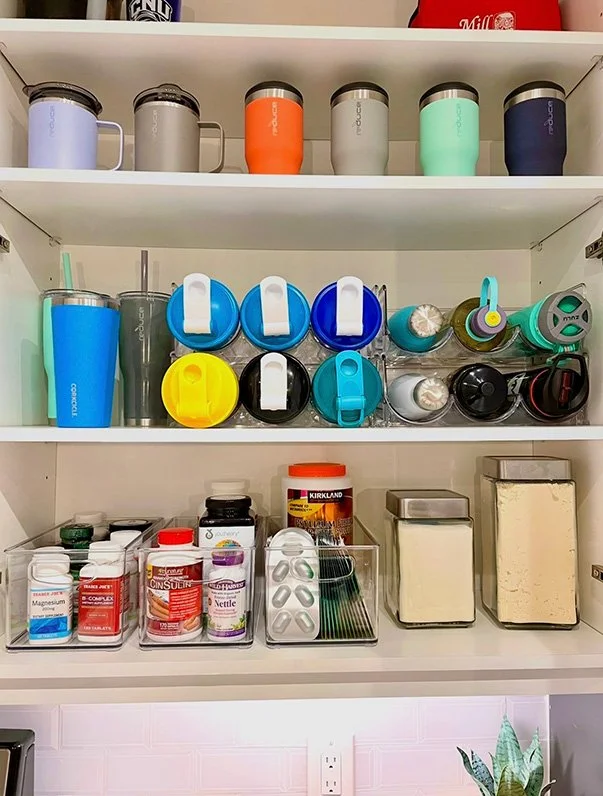 Kitchen cabinet shelf with tumblers, water bottles, spice containers, and supplement jars.