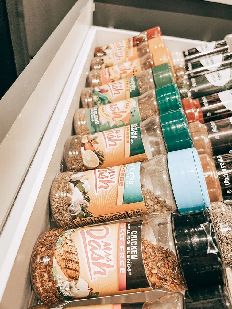 A selection of seasoning jars on a shelf, including chicken salt, herb, and garlic seasoning.