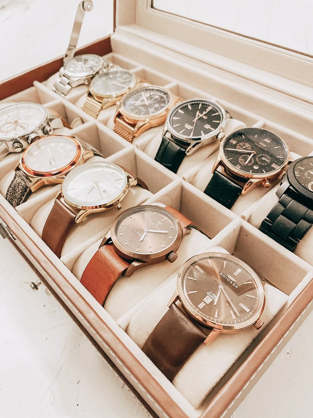 A collection of men's wristwatches in a display case, with various styles and band materials, neatly arranged in individual compartments.