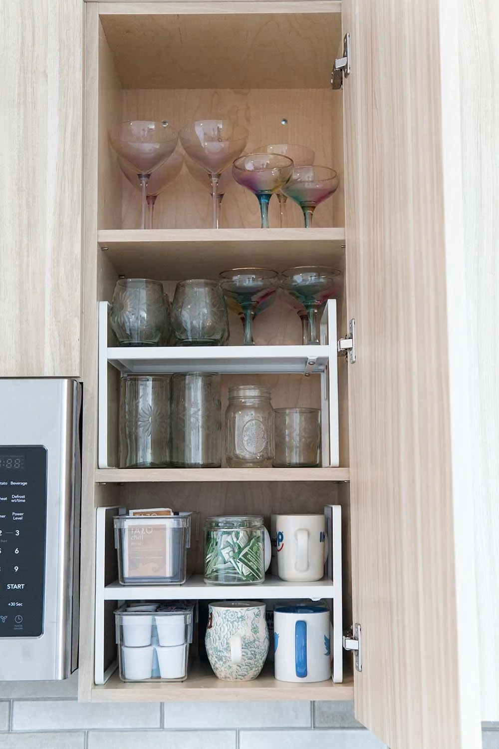 Open kitchen cabinet with upside-down glassware, mugs, and containers.
