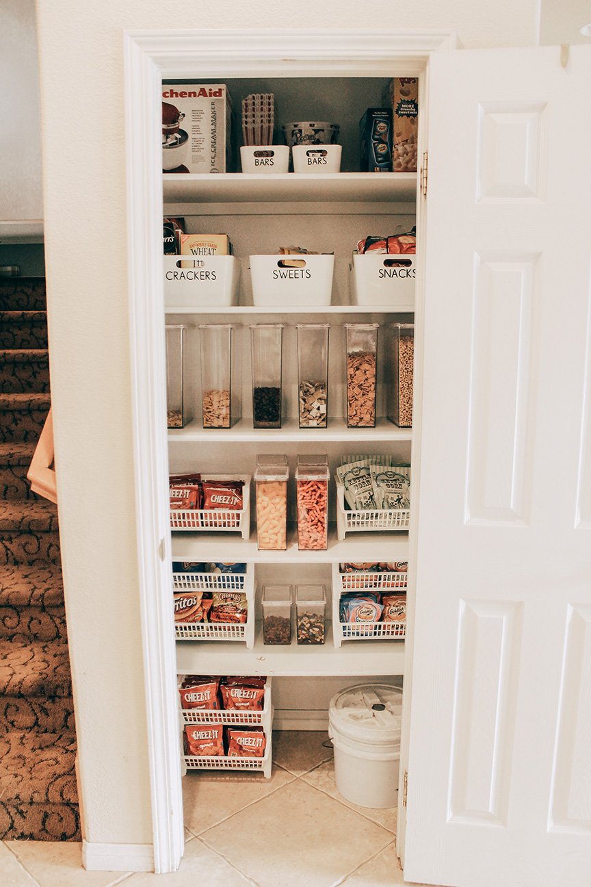 Pantry with snacks, cereals, and baking supplies organized in white bins and clear containers.